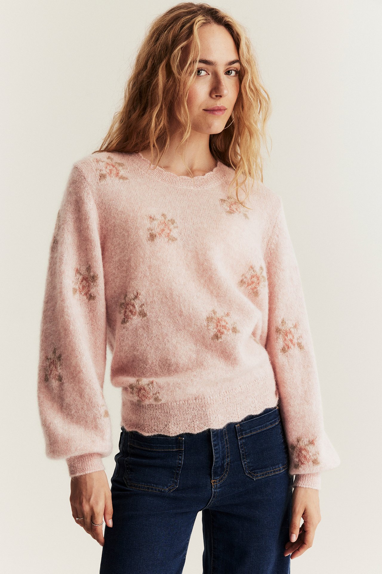 Front view of a woman wearing a pink floral mohair blend sweater and dark blue jeans.
