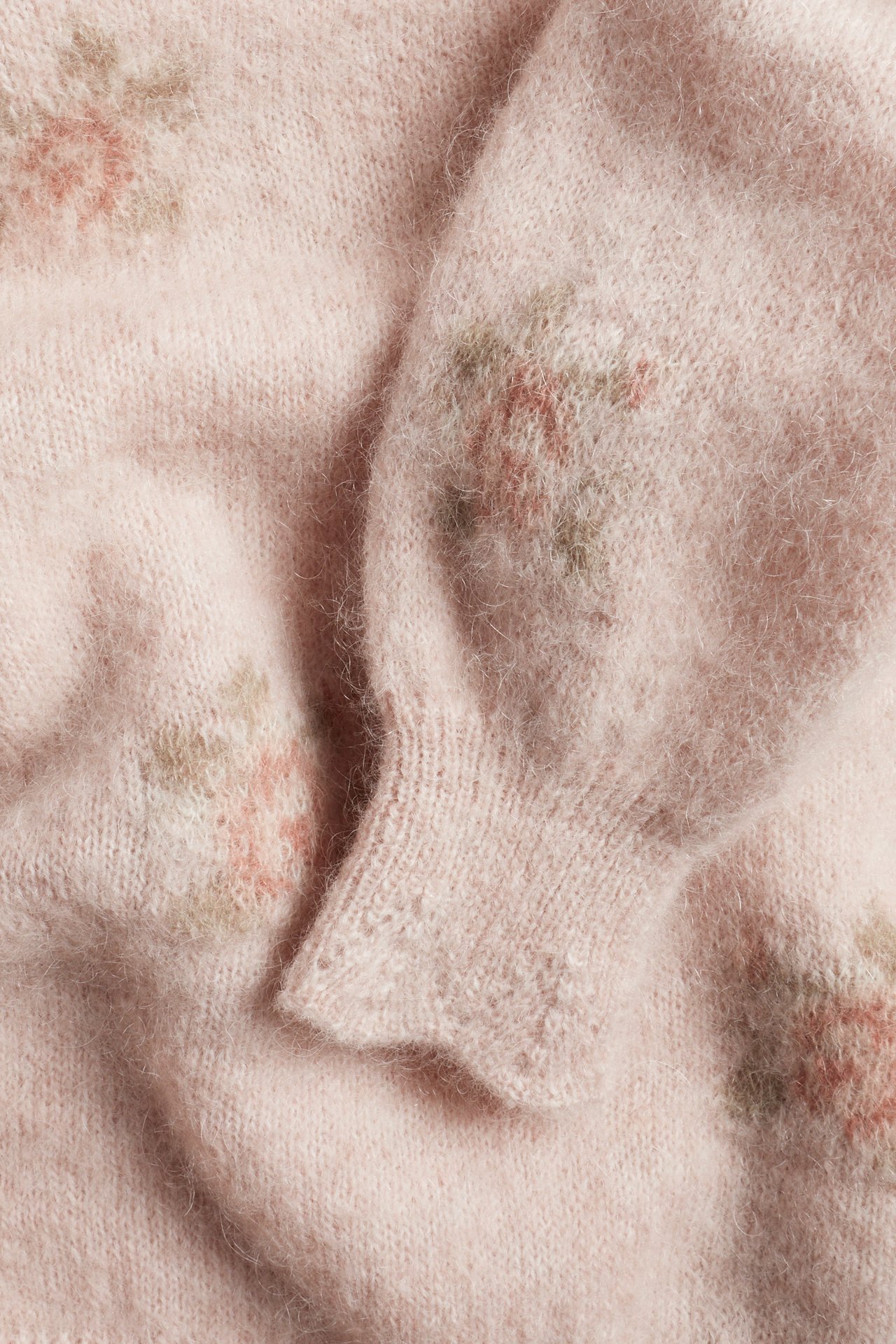 Close-up of a pink mohair-blend knitted sweater with jacquard floral pattern and ribbed cuffs with lace edge.