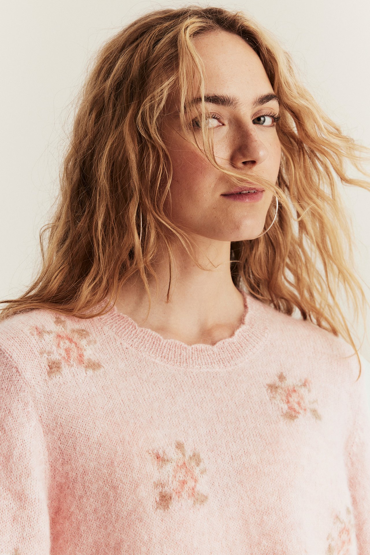 Close-up of woman in a pink floral wool blend sweater with scalloped neck and silver hoop earrings.