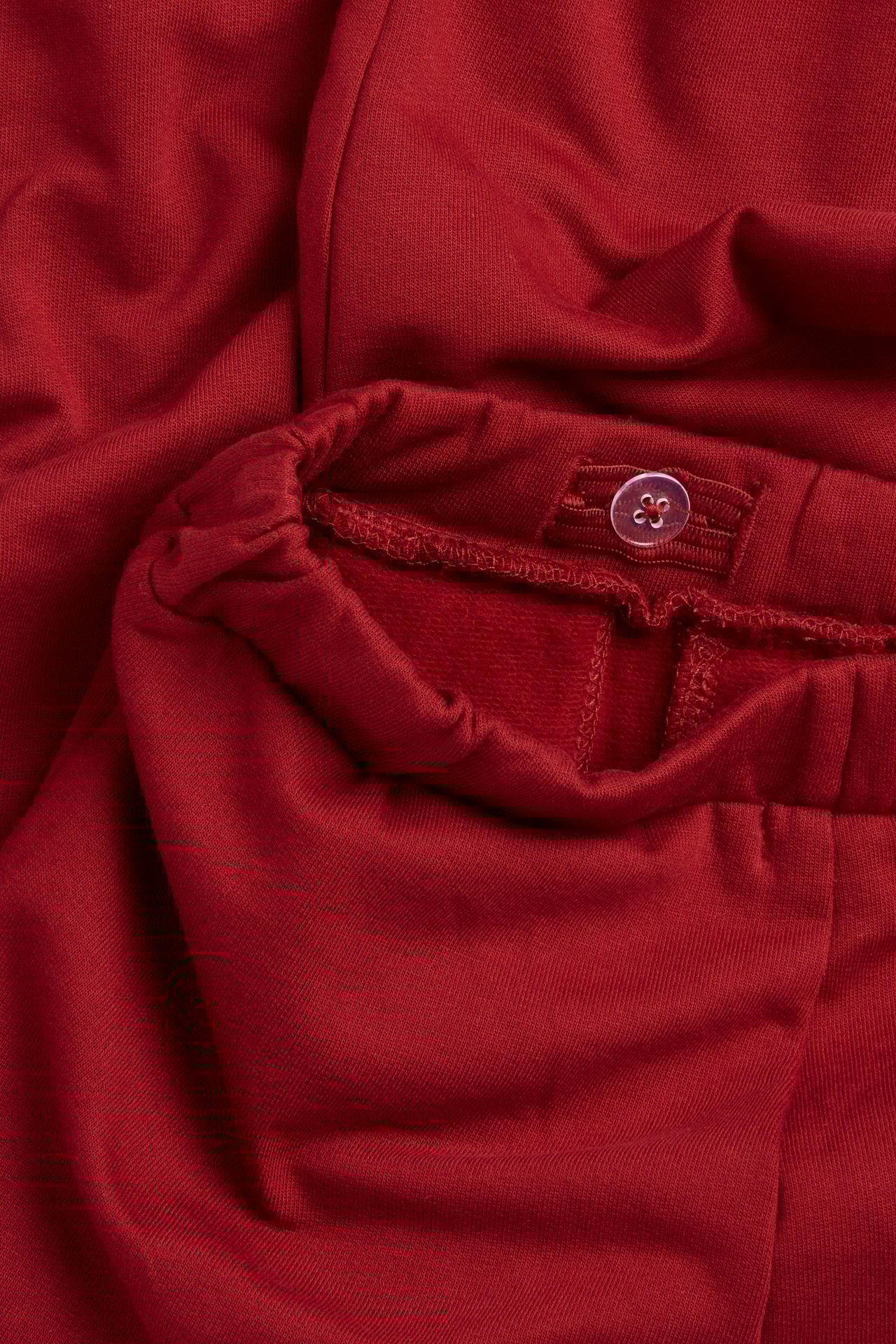 Close-up of red cotton jogging pants with an elastic waistband and a clear decorative button.