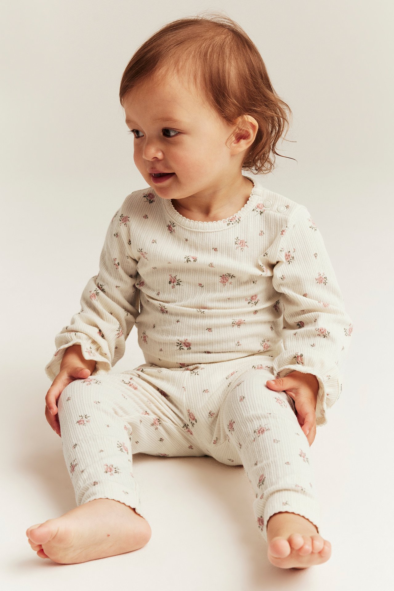 Front view of a baby wearing an off-white ribbed floral long-sleeved bodysuit with shoulder snaps and matching leggings.