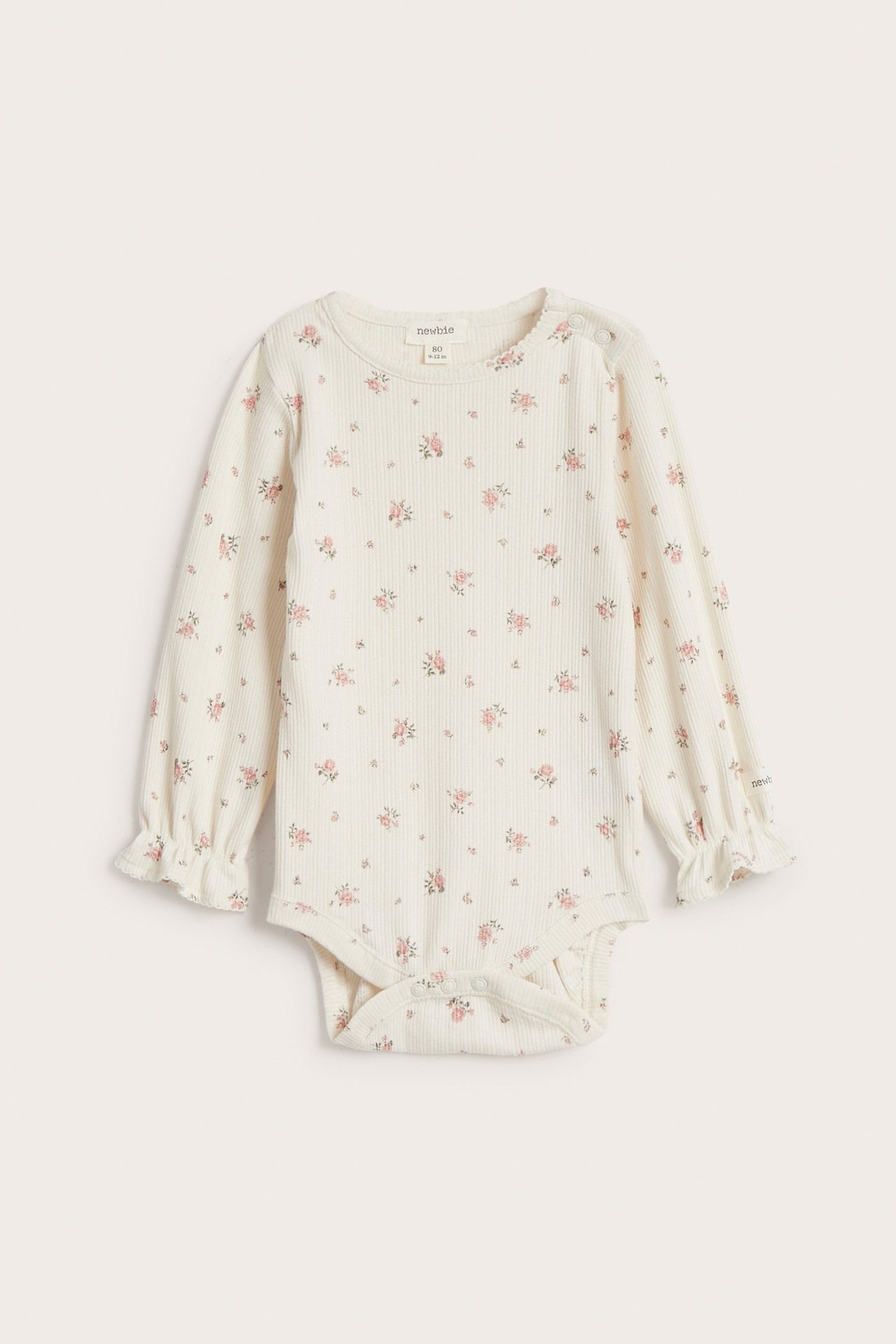Vorderansicht: Cremefarbener gerippter Baby-Body mit rosa Blumenmuster, langen Rüschenärmeln und Picot-Ausschnitt.