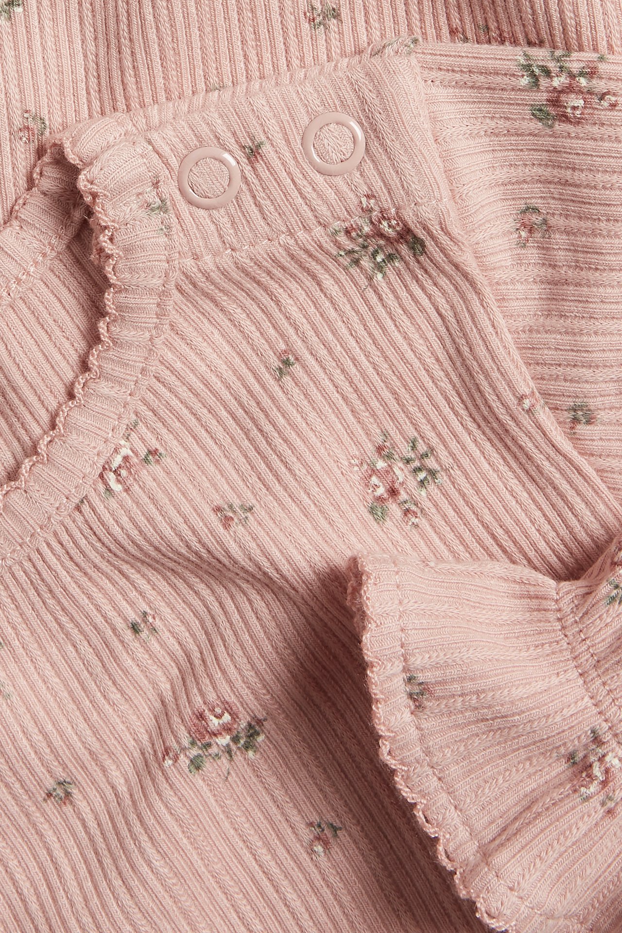 Nahaufnahme eines rosa gerippten Baby-Bodys mit Blumenmuster, Picot-Rand und Druckknöpfen.