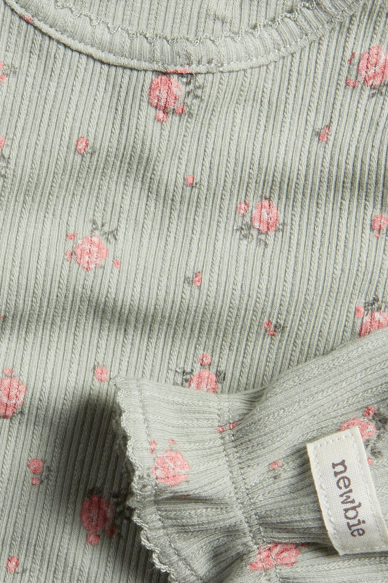 Nahaufnahme: grüner gerippter Baby-Body mit rosa Blumenmuster, Picot-Besatz und Rüschenärmel.