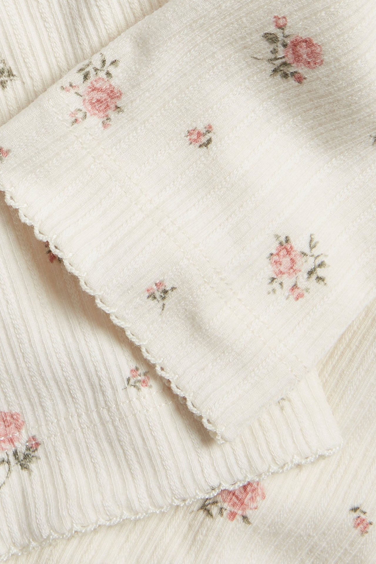 Nahaufnahme von cremeweißen gerippten Leggings mit rosa Blumenmuster und Picot-Saum am Beinabschluss.