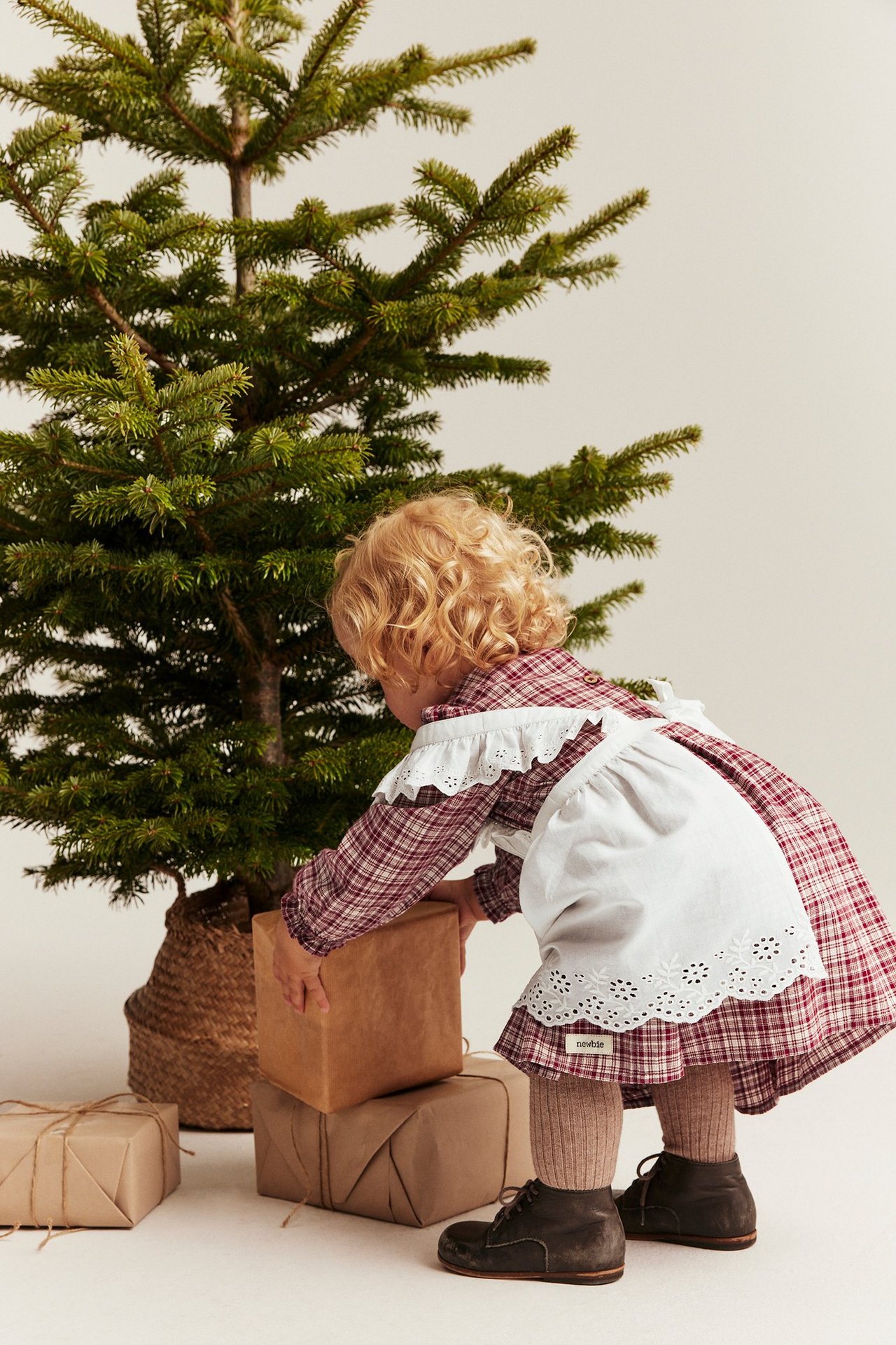 Back view of a kid in a red checked cotton dress with a white embroidered apron.