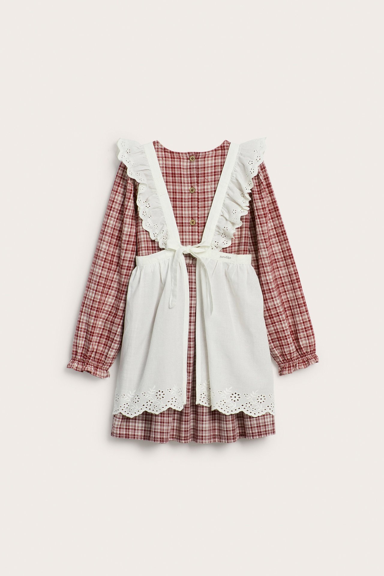 Front view of a kid's red checkered cotton dress with ruffles, worn under a white eyelet apron.