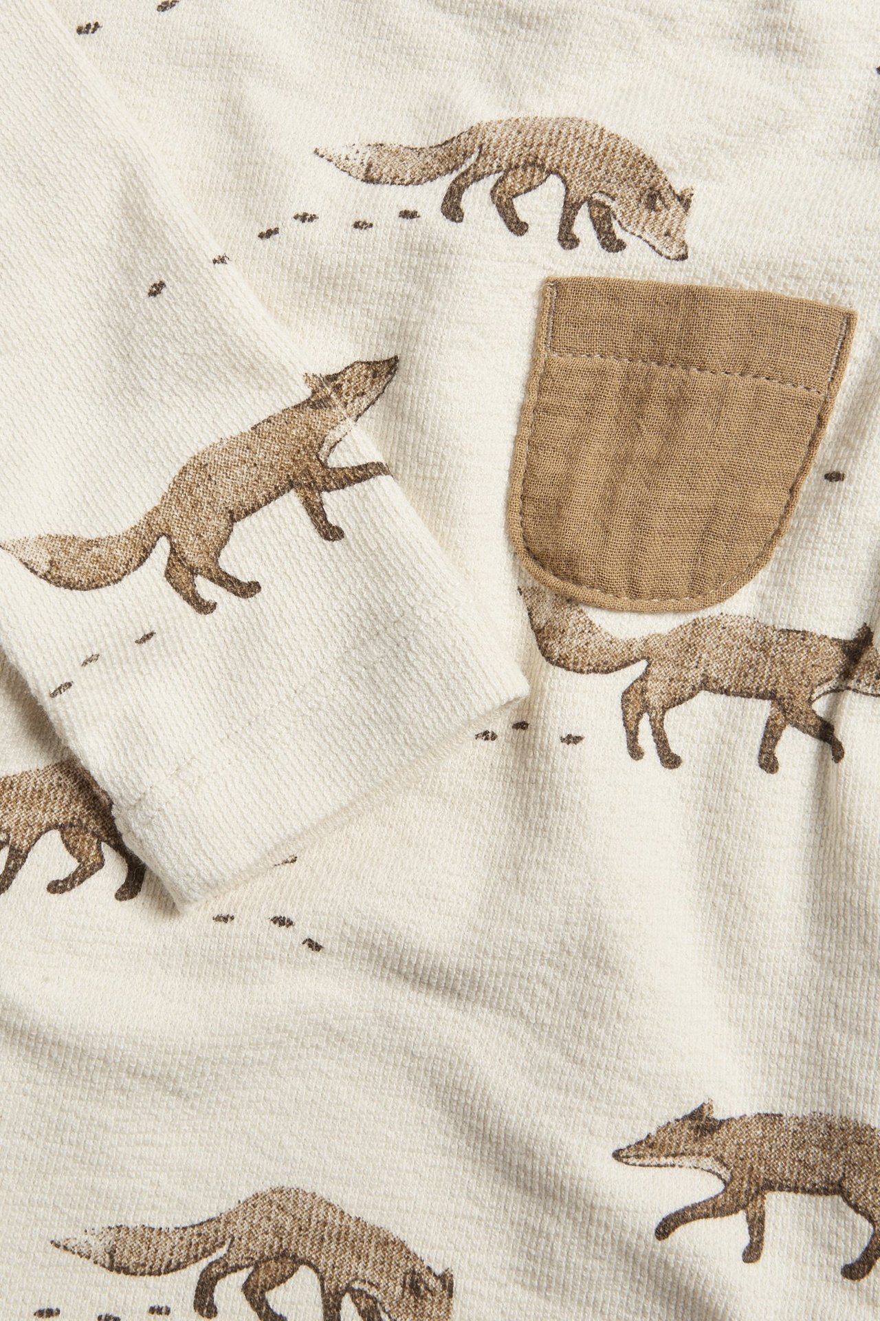 Nahaufnahme eines hellbeigen langärmeligen Babybodys mit braunem Fuchsdruck und einer kleinen Brusttasche.