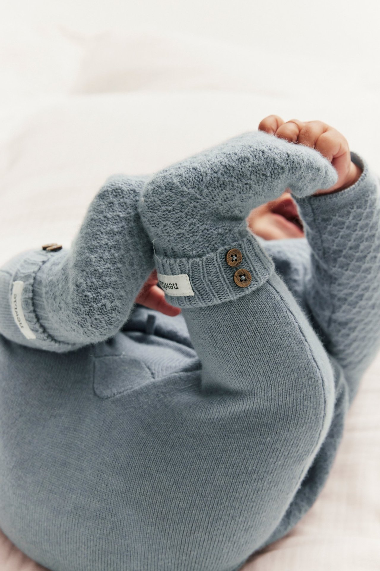 Close-up of baby in light blue knitted wool-cashmere pants and matching textured top with buttons.