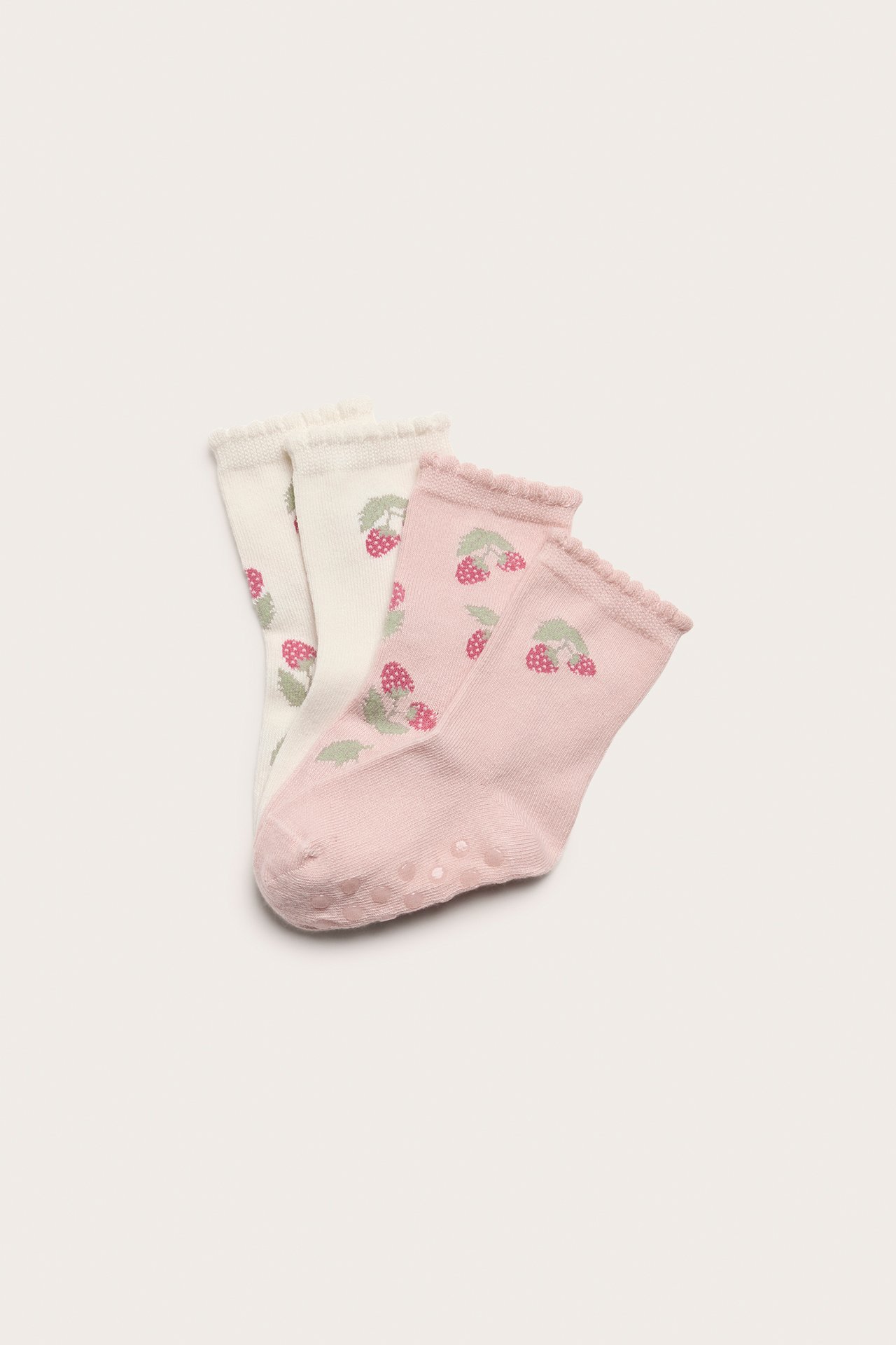 Top-down view of four baby socks: two off-white, two pink, with strawberry patterns, scalloped edges, and anti-slip.