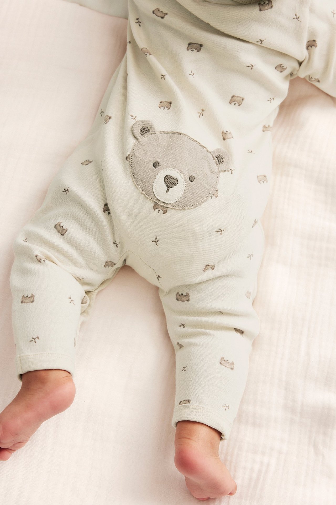 Close-up of a baby wearing light beige cotton pyjamas with a brown bear pattern and a large grey bear application.