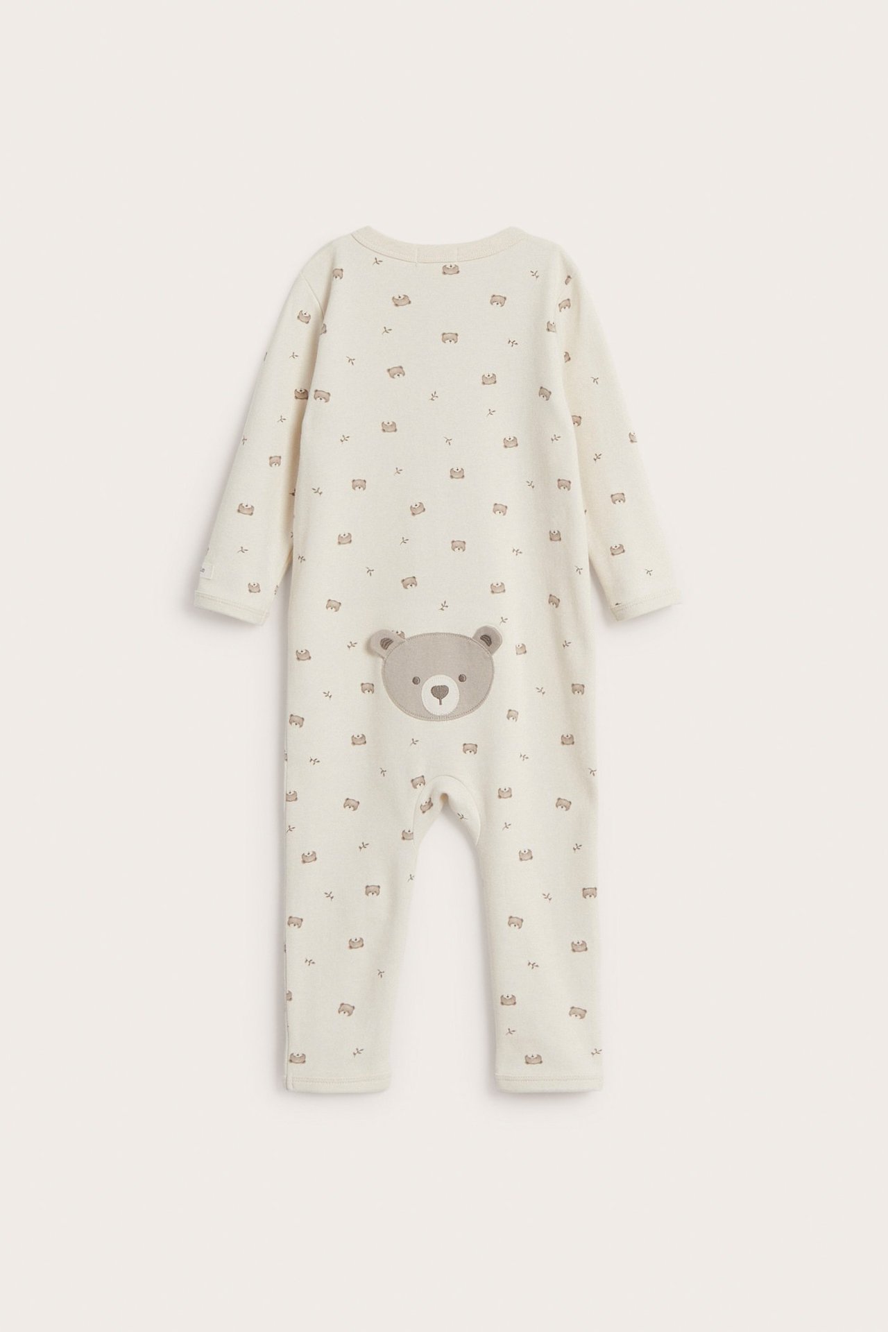 Back view: light beige cotton baby pyjamas with small bear pattern and a large bear application.