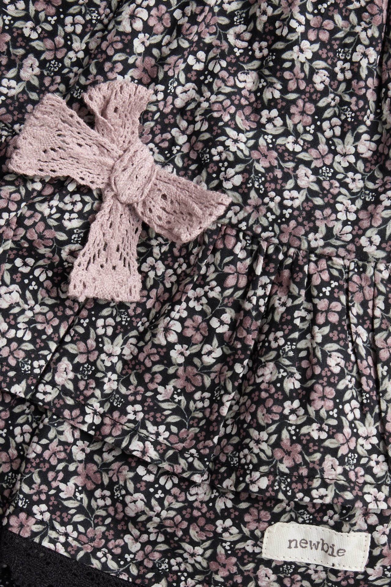 Close-up of a black floral cotton skirt with ruffles and a pink knitted bow.