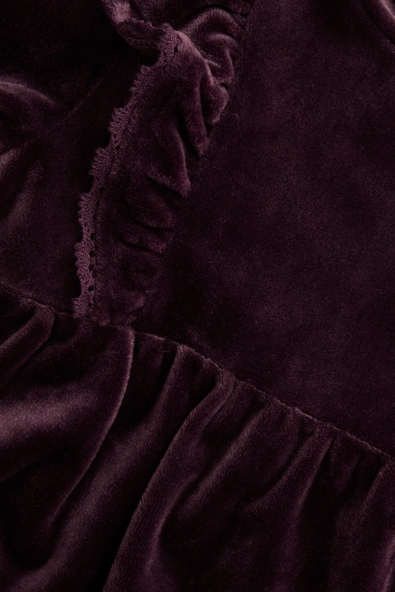 Nahaufnahme eines pflaumenfarbenen Velourskleides mit Rüschen und Spitzenbesatz.
