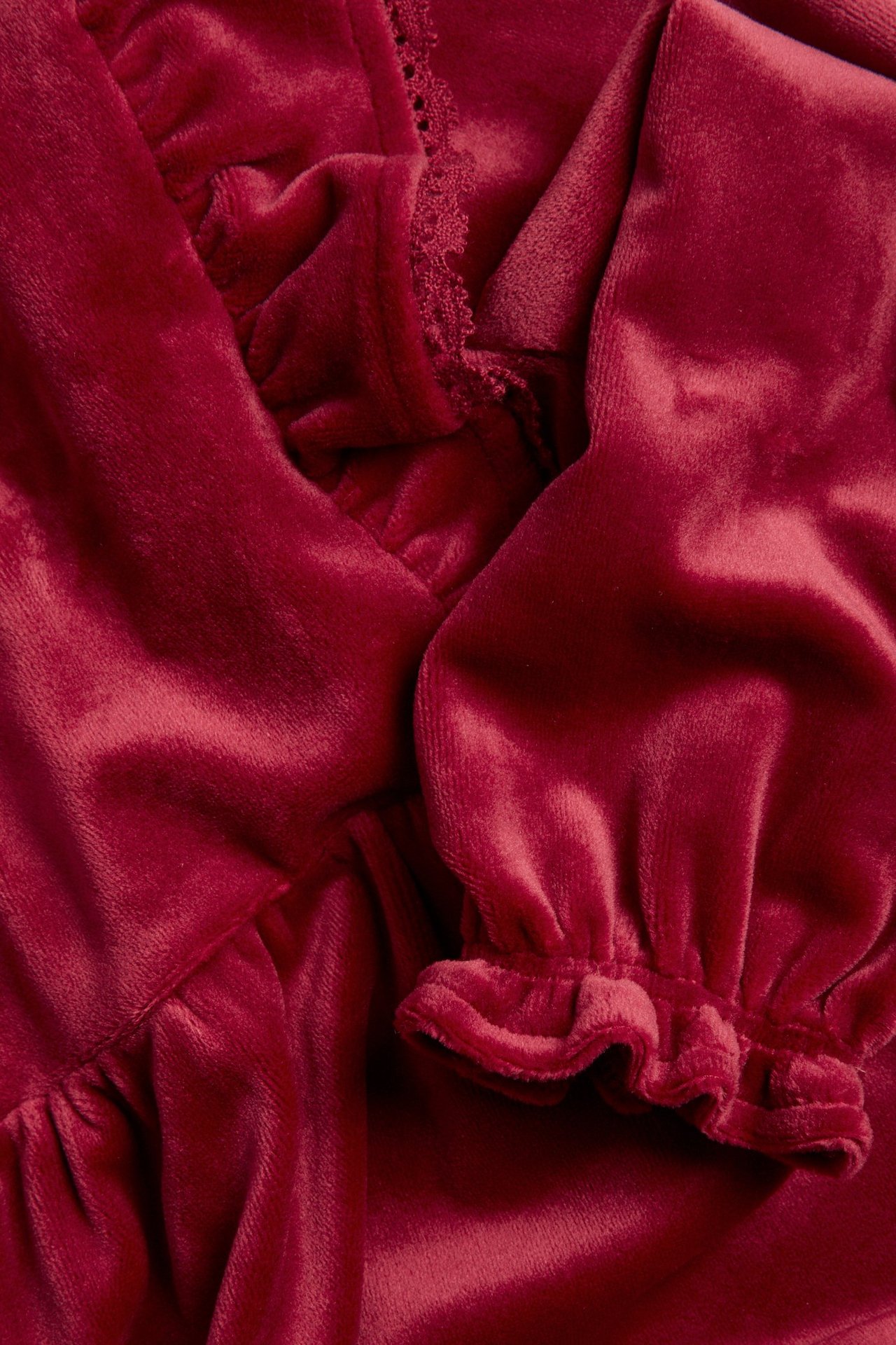 Close-up of a kid's red velour dress with ruffled shoulders, lace trim, and elastic ruffled cuffs.