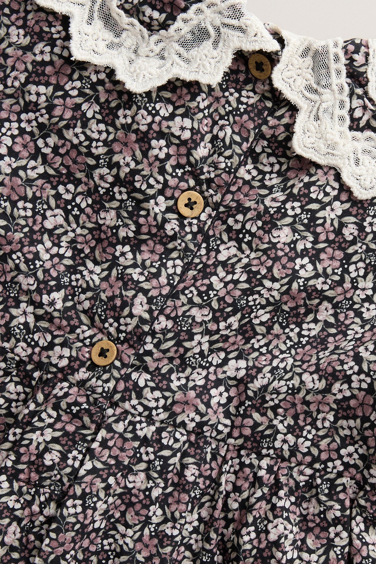 Nahaufnahme eines schwarzen geblümten Baumwollkleides mit weißem Spitzenkragen und Holzknöpfen.