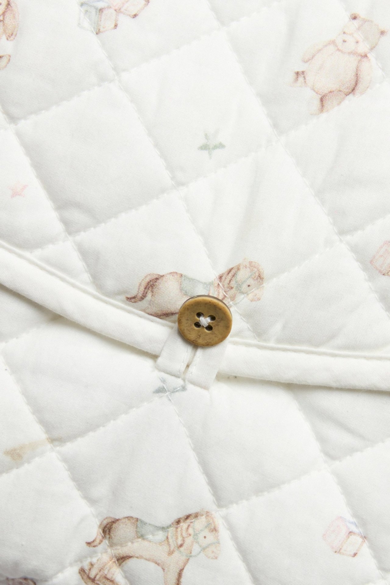 Close-up of an off-white quilted foldable changing mat with a toy pattern and wooden button.