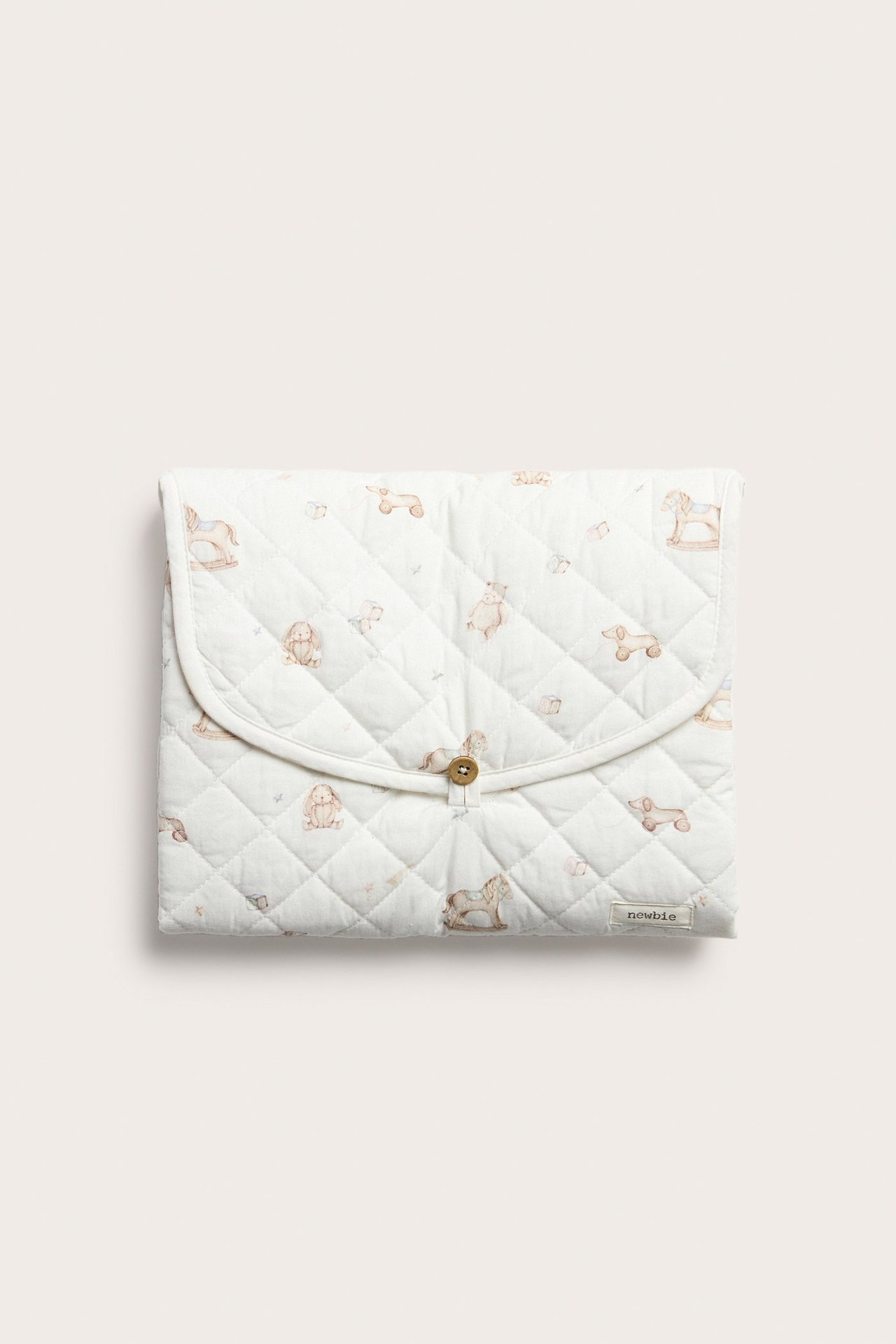 Front view of an off-white quilted foldable changing mat with a toy pattern and button closure.