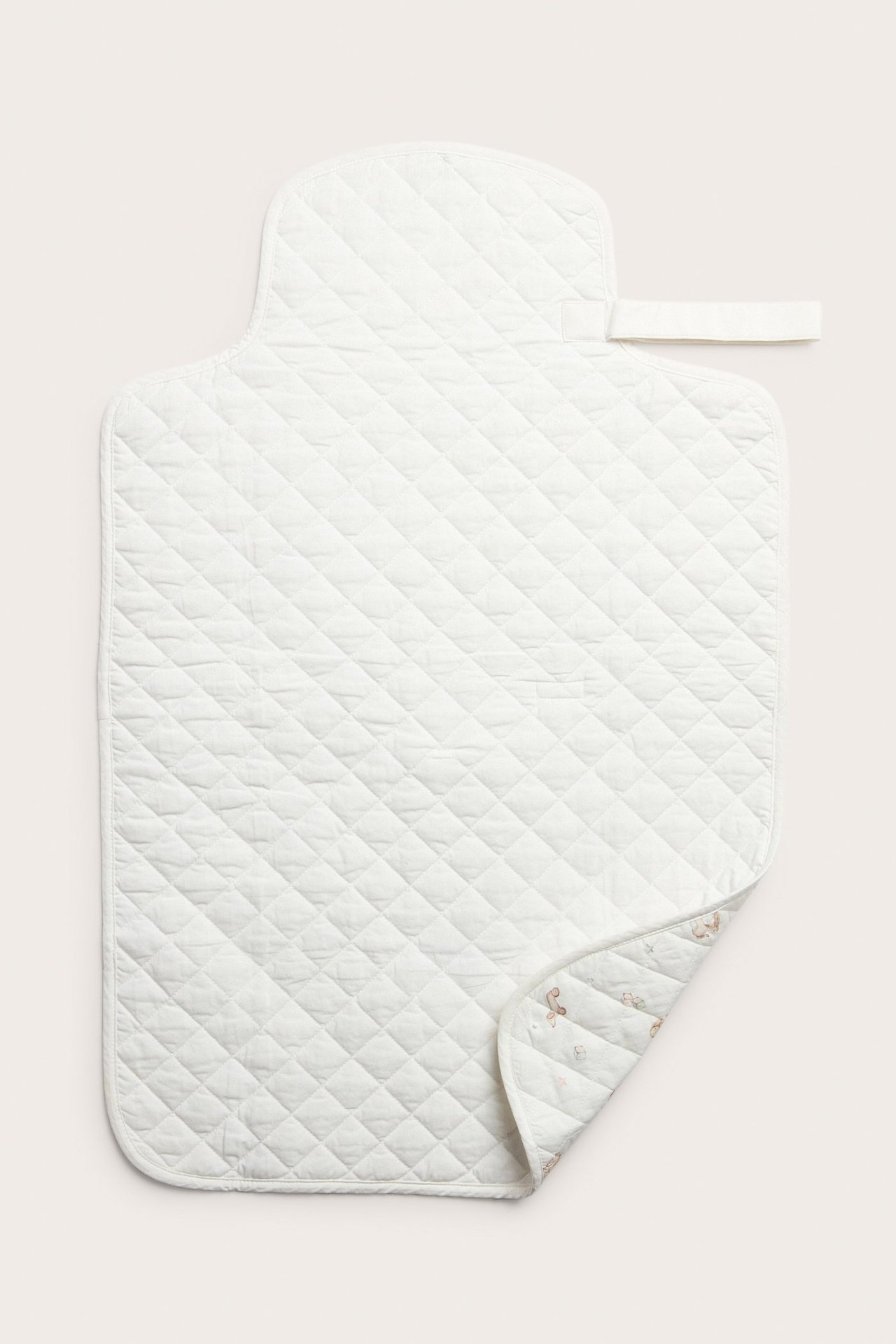 Top view of an off-white quilted foldable changing mat with a handle and a patterned underside.