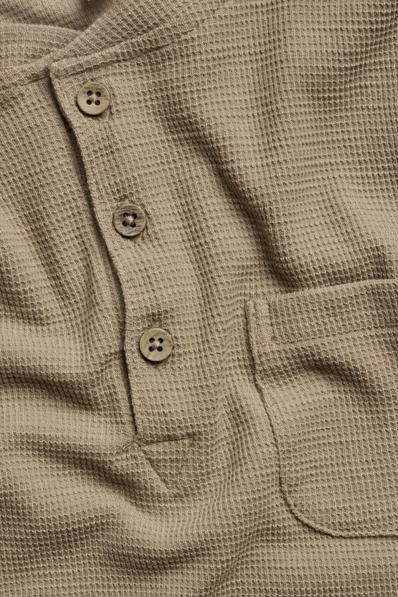 Nahaufnahme eines beigen Waffelstrick-Henleyshirts mit Dreiknopfleiste und Brusttasche.