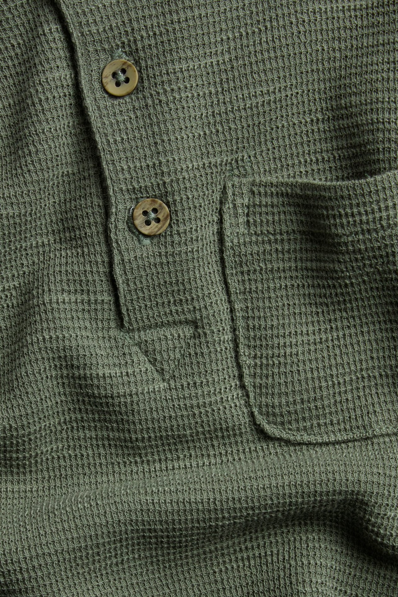 Nahaufnahme eines grünen Waffelstrick-Langarm-Henleyshirts mit zwei Holzknöpfen und einer Brusttasche.