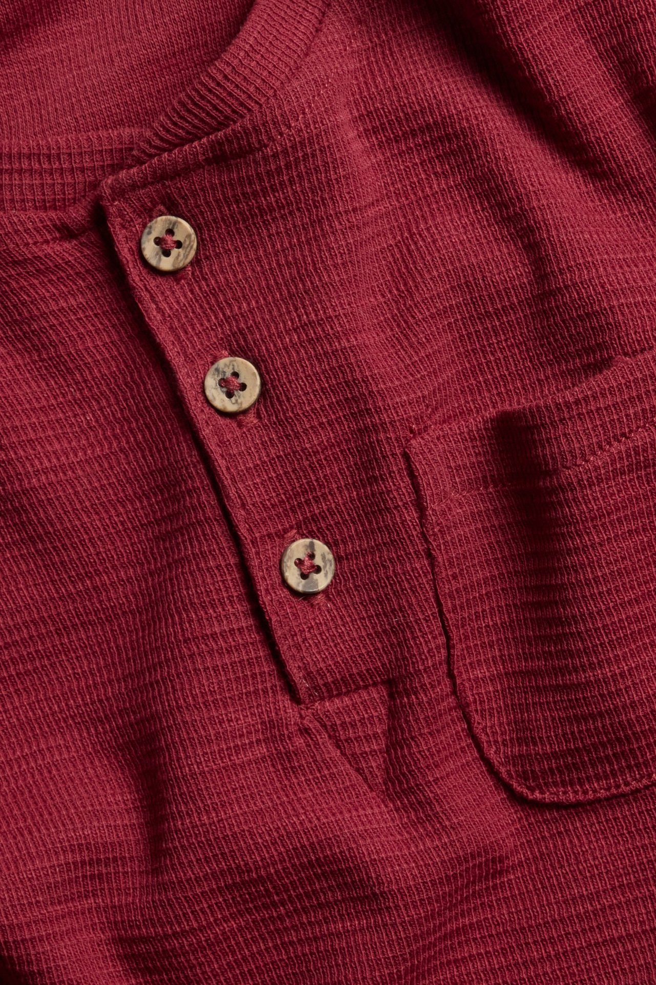 Close-up front view of a red cotton waffle-textured henley shirt with a three-button placket and chest pocket.