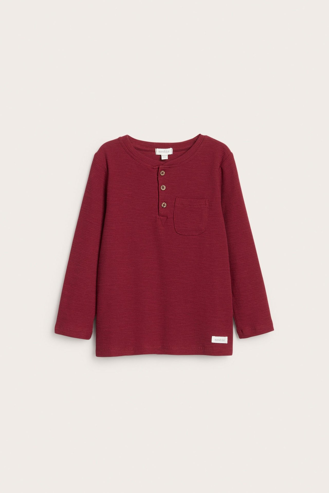 Front view of a kid's red waffle-knit long-sleeved Henley shirt with button placket and chest pocket.