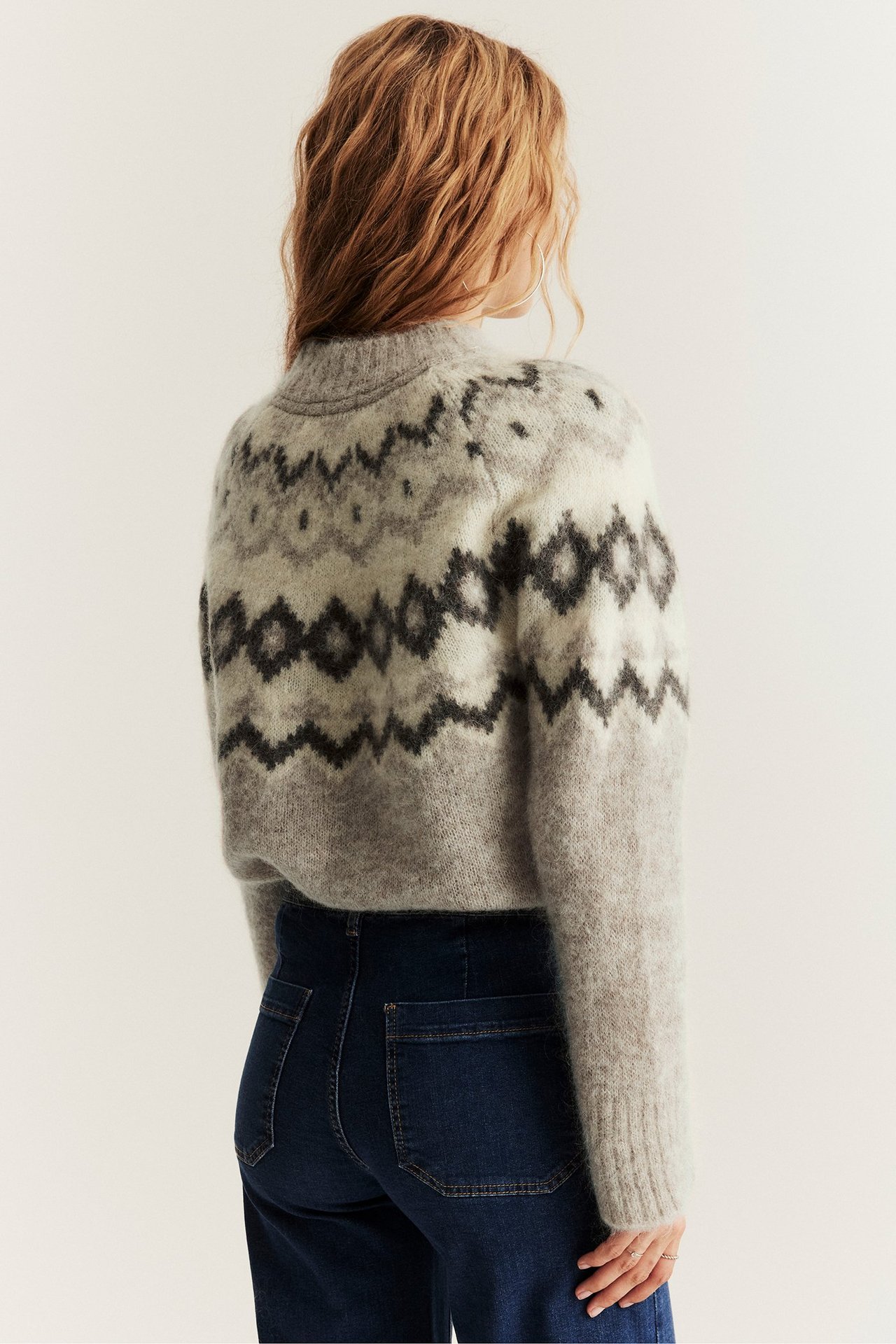 Rückenansicht einer Frau in hellgrau meliertem Wollmix-Jacquardpullover und dunkelblauen Jeans.