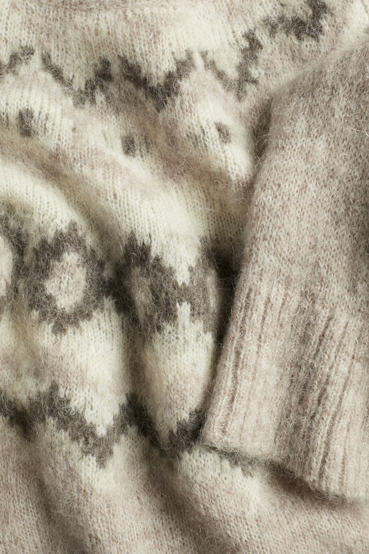 Nahaufnahme eines beigefarbenen Melange-Strickpullovers mit dunklem Jacquardmuster und glattem Ärmel.