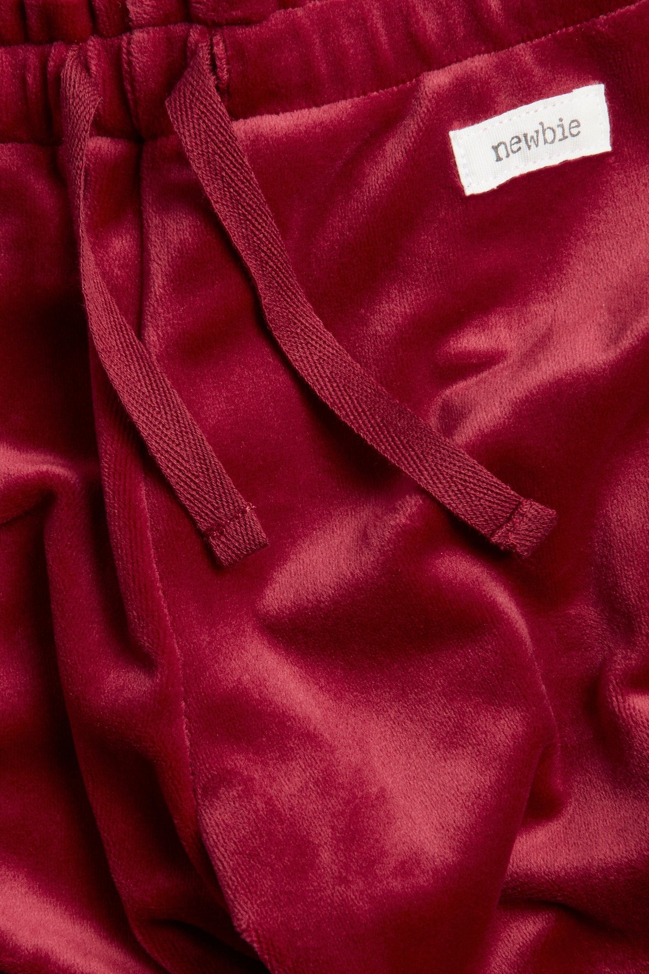 Close-up of red velour jogging bottoms with an elasticated drawstring waist and a "Newbie" label.