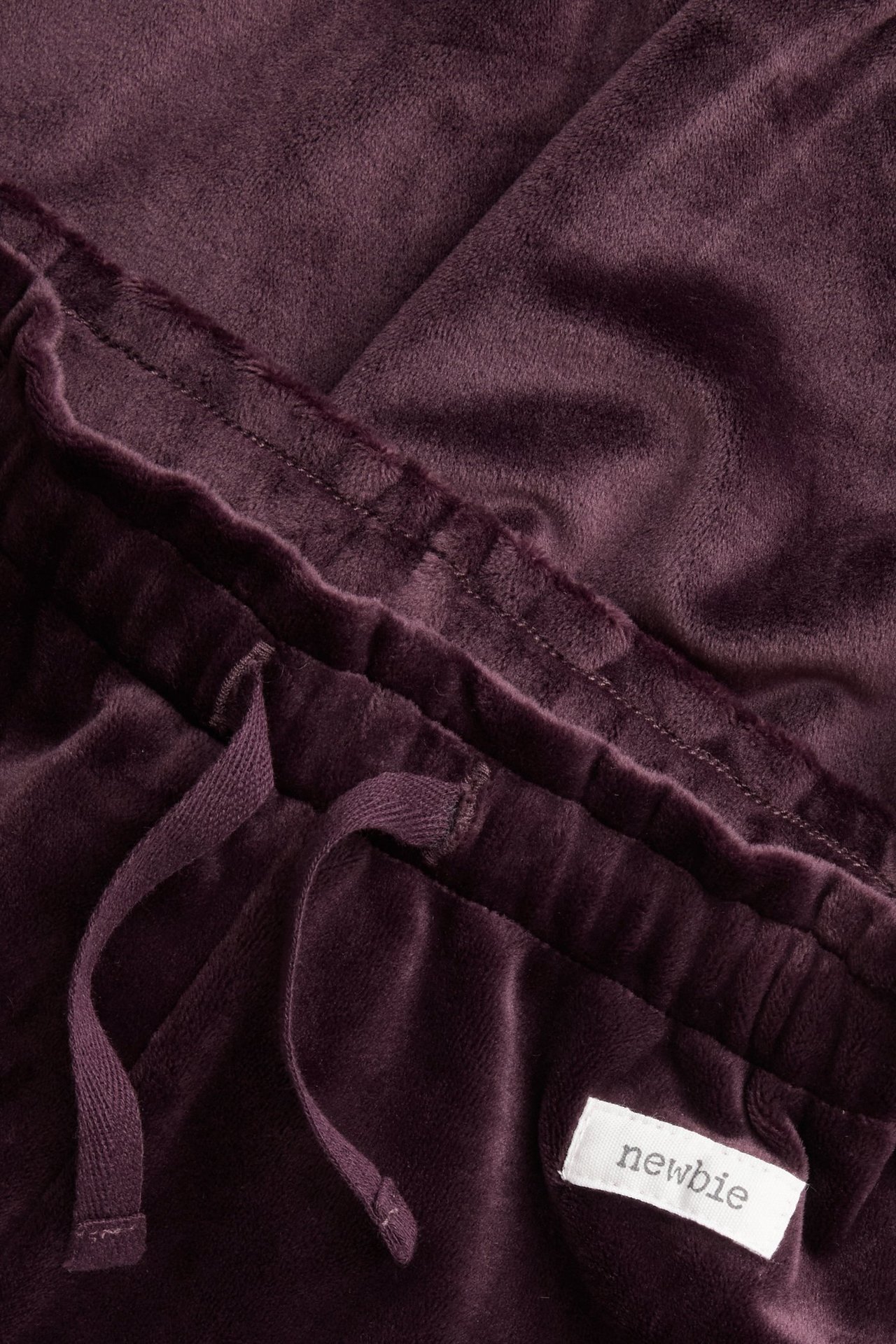 Nahaufnahme lila Velours-Jogginghose mit elastischem Bund, Kordelzug und einem weißen "newbie"-Etikett.