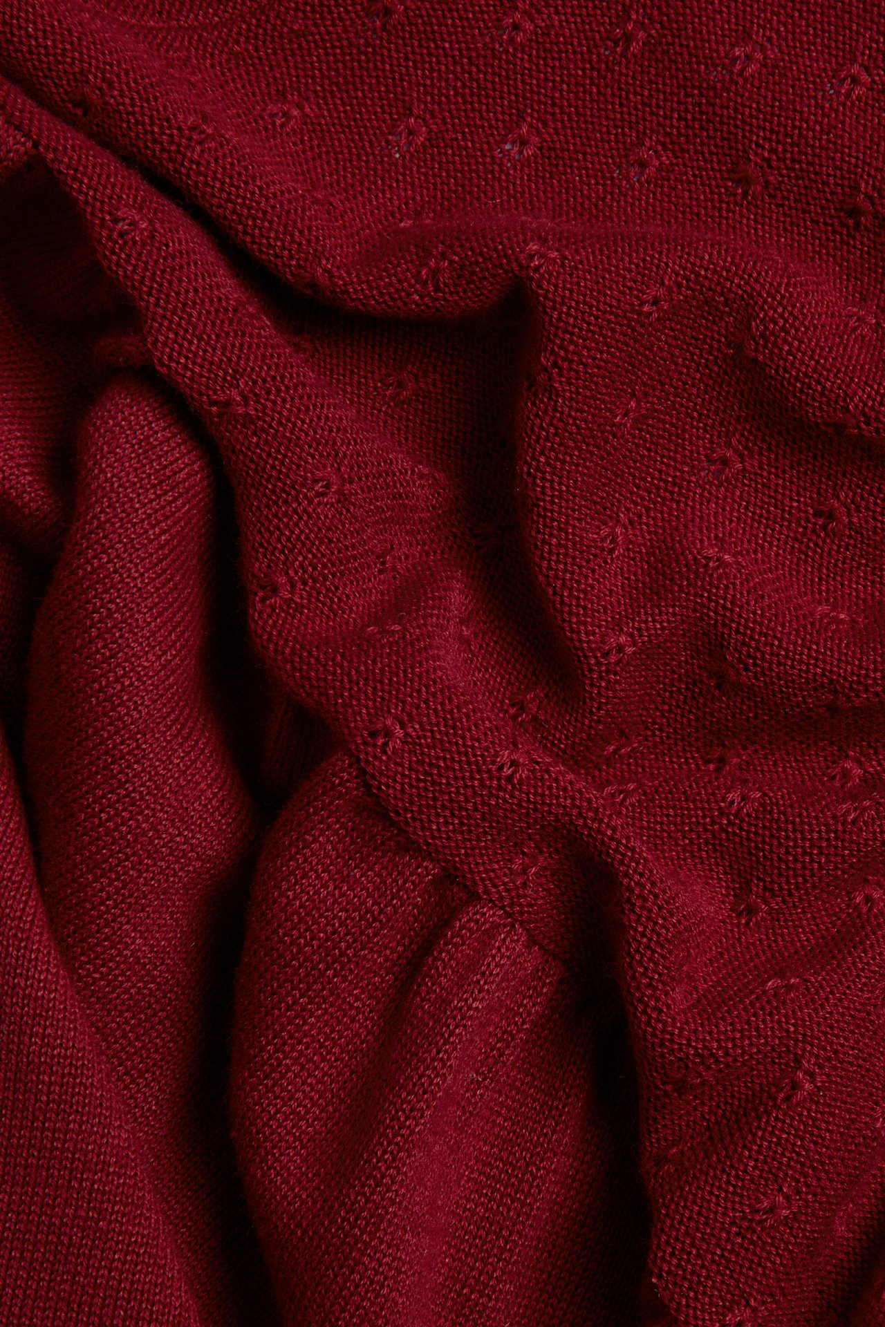 Nahaufnahme von rotem gestricktem Baumwollstoff vom Kleid, mit dezentem gesticktem Punktmuster.