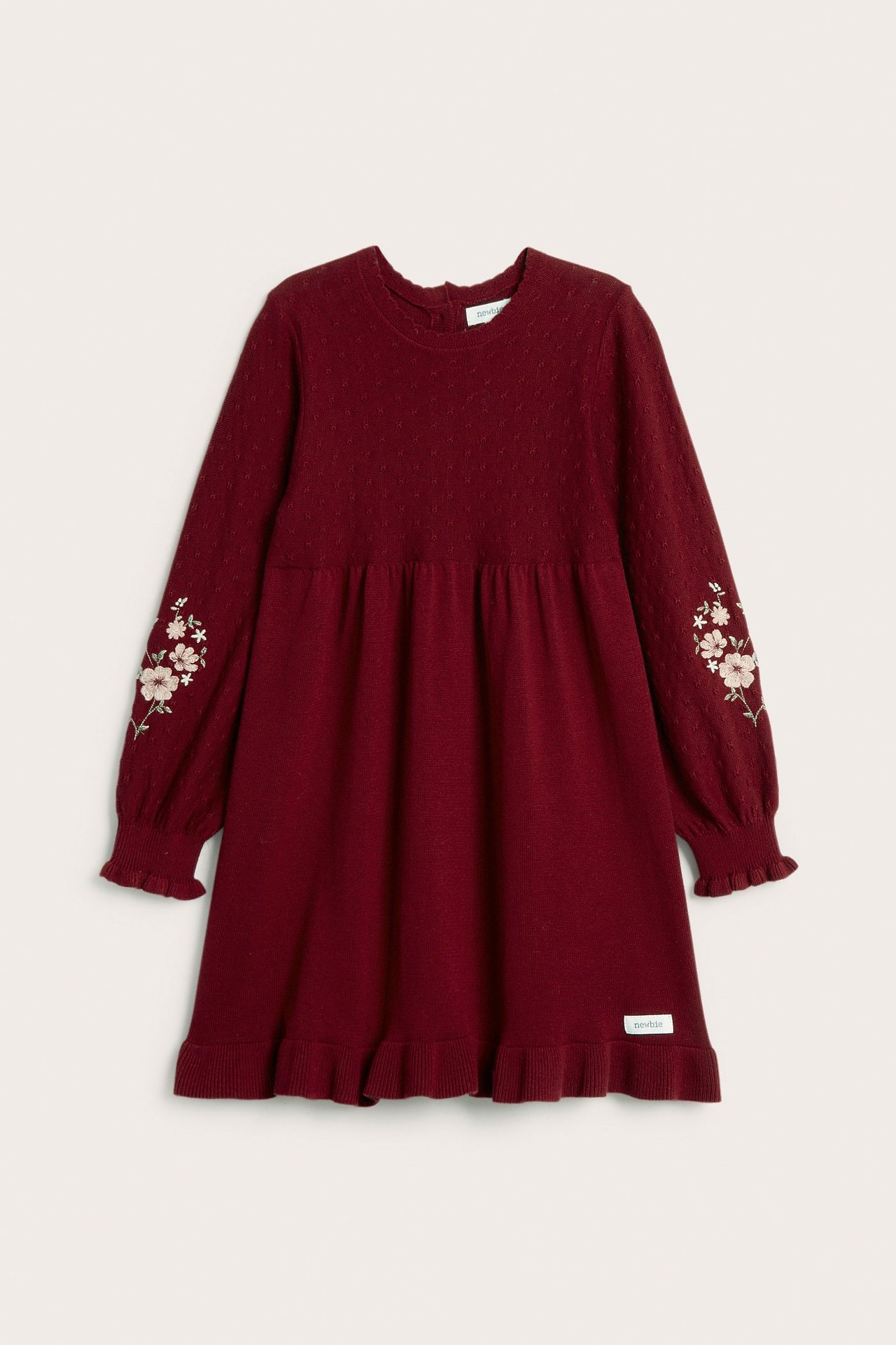 Front view of a kid's red knitted cotton dress with embroidered floral sleeves, ruffle hem, and back buttons.