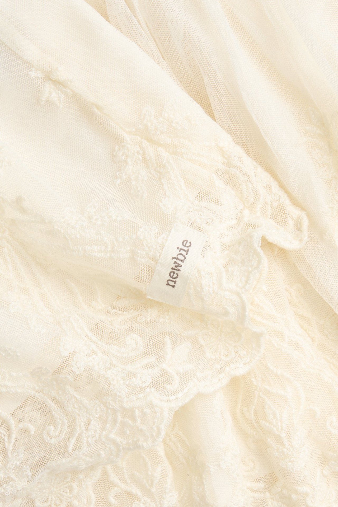 Close-up of a light beige embroidered mesh skirt with a visible "newbie" tag.