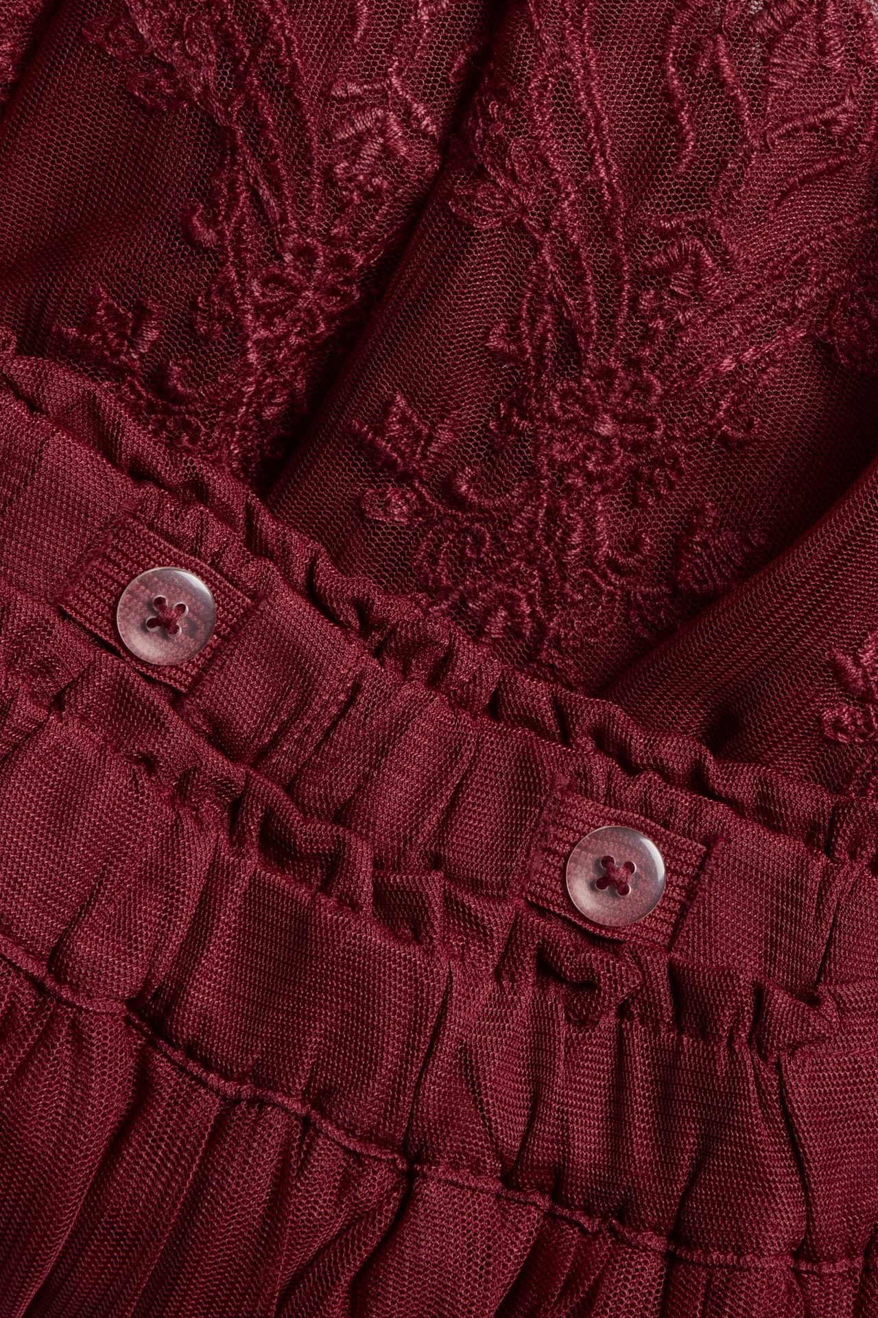 Close-up: red embroidered mesh kid's skirt, adjustable elastic waistband, clear buttons.