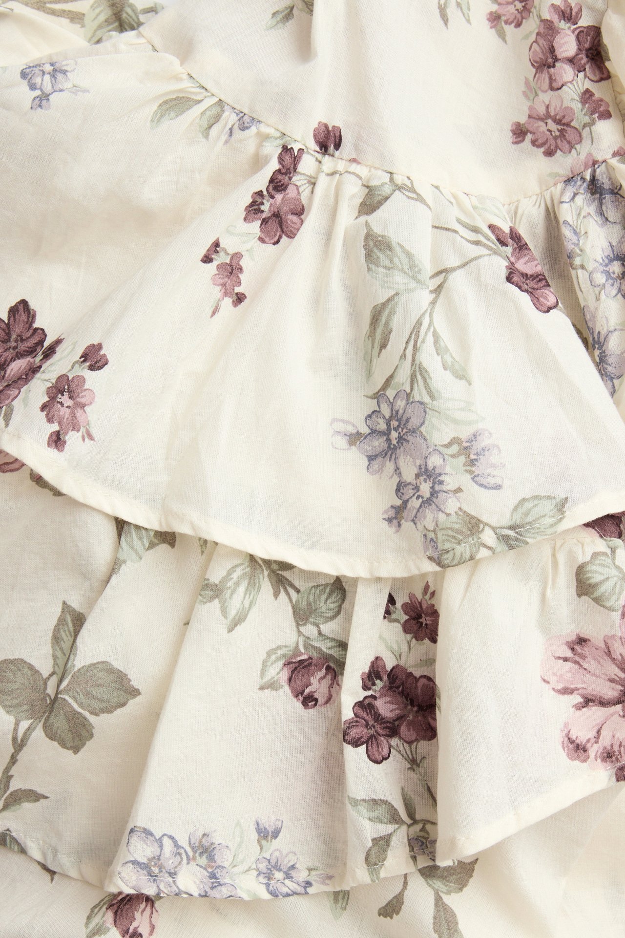 Close-up of a light beige cotton blouse with purple and green floral pattern and ruffles.