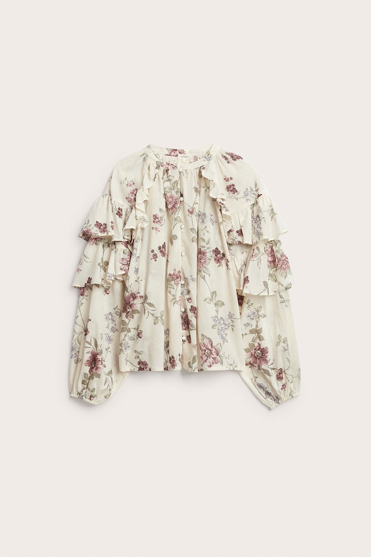 Front view of a light beige cotton blouse with purple floral pattern, ruffles, and covered buttons.