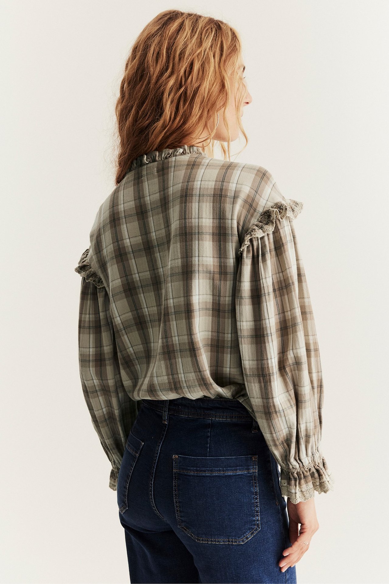 Rückenansicht einer Frau in beiger karierter Baumwollbluse mit Rüschen und dunkelblauer Jeans.