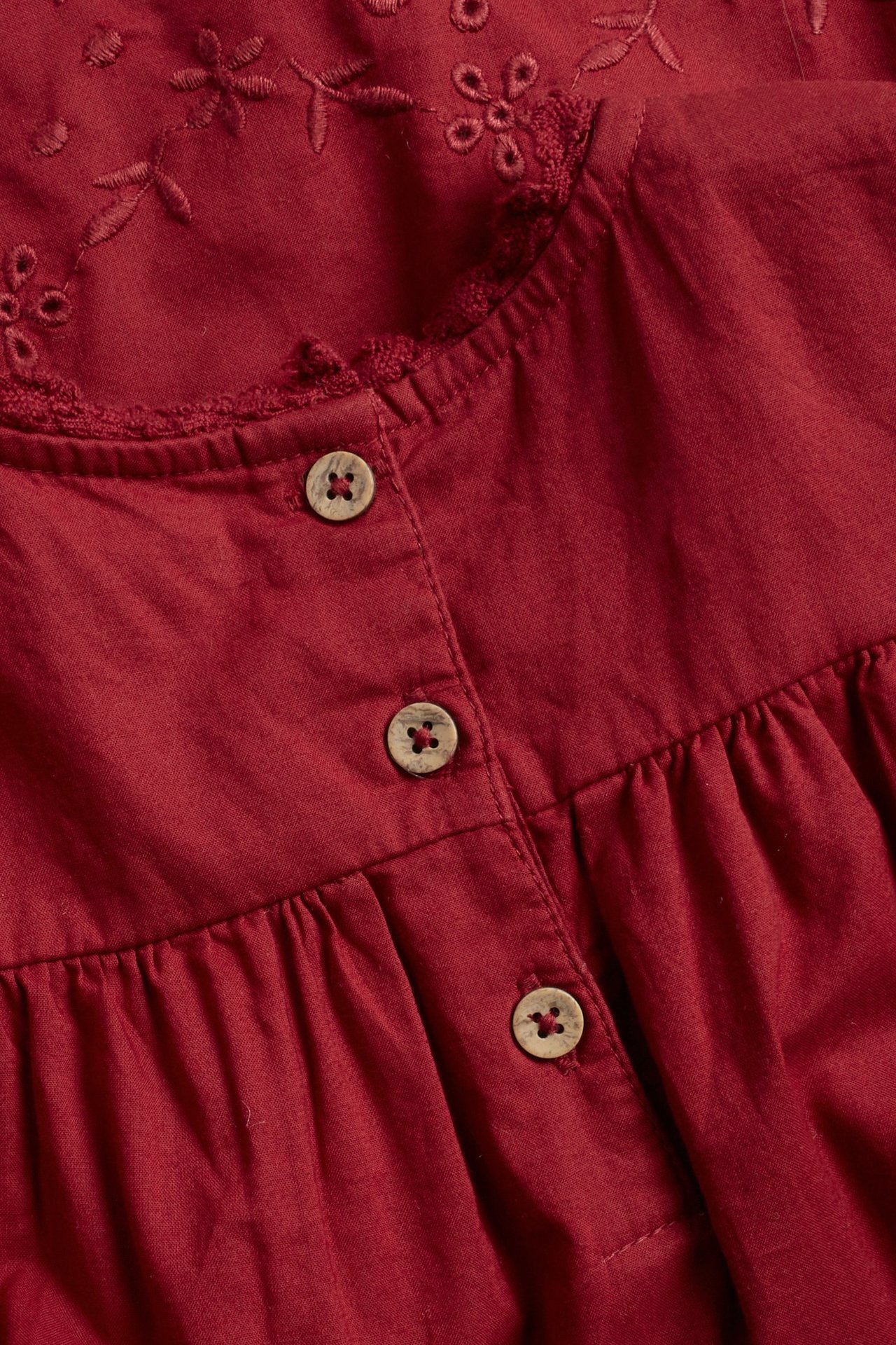Close-up of a red cotton dress with wooden buttons and floral embroidery on the yoke.