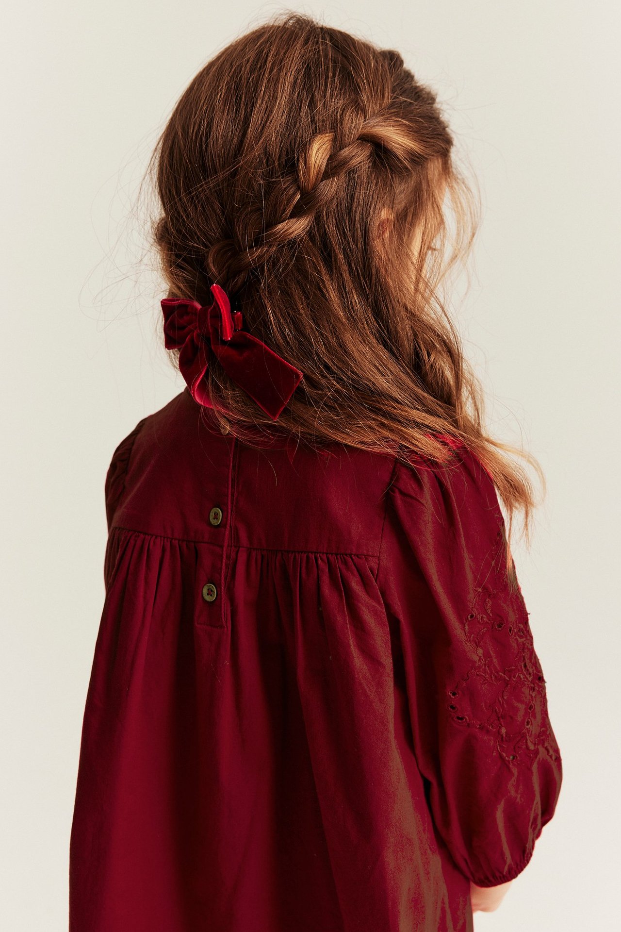 Back view: Kid wears red woven dress, embroidered sleeves, back buttons. Red velvet hair bow.