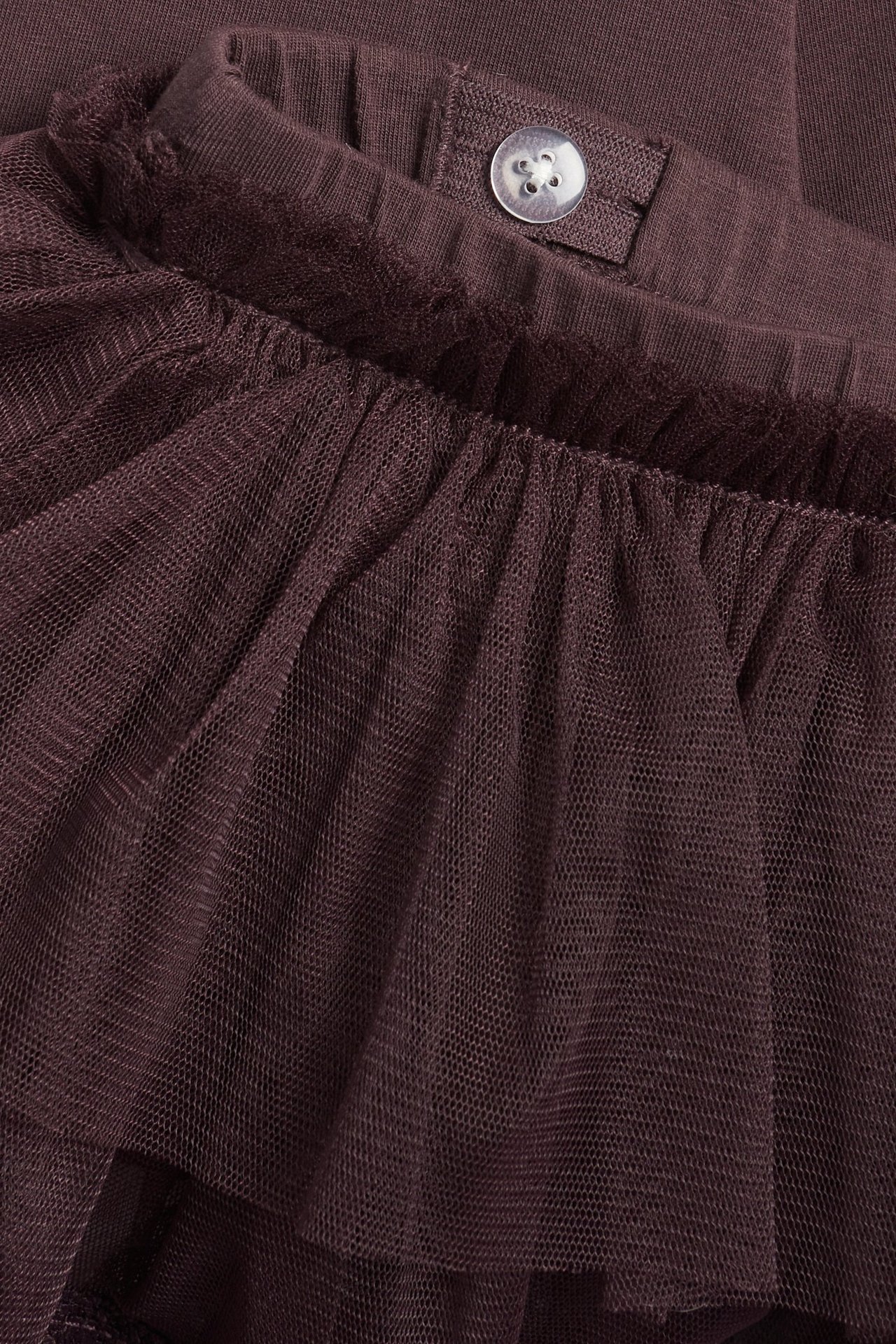 Close-up of kid's dark plum leggings with an attached ruffled tulle skirt and adjustable elastic waistband with a button.