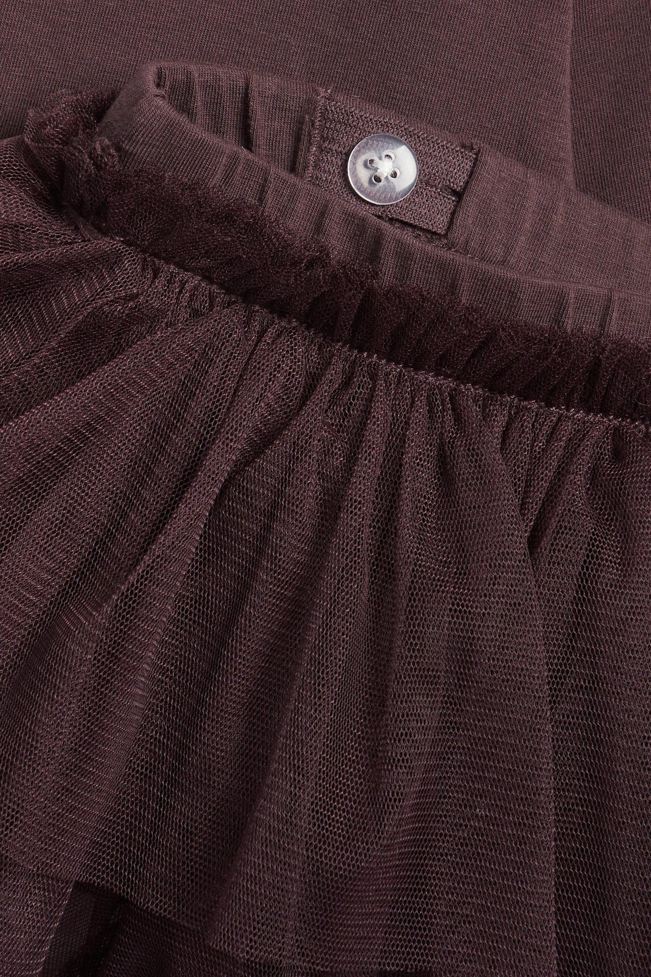 Close-up of dark purple cotton leggings with an attached ruffled tulle skirt and a waist button.