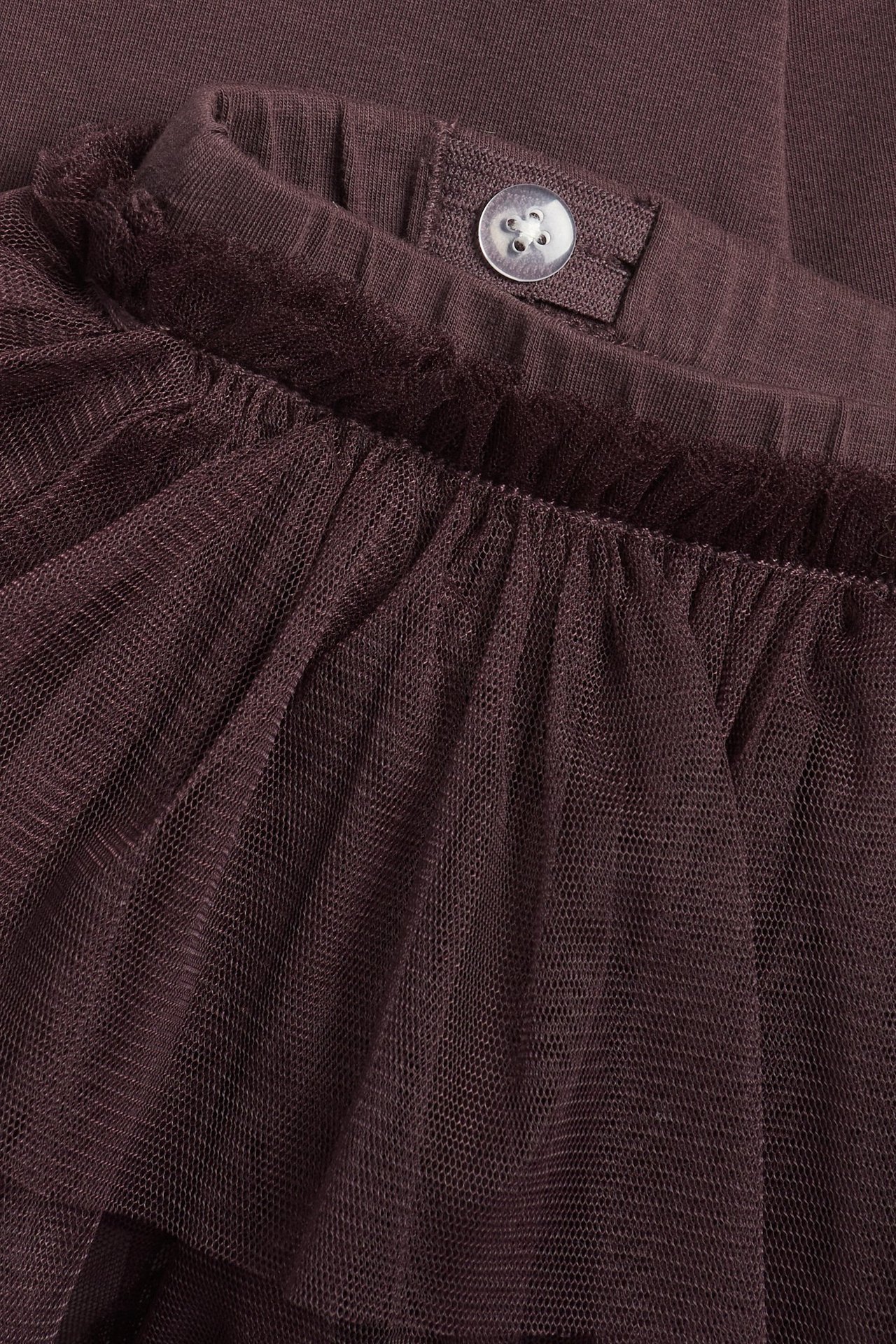 Nahaufnahme von dunkelvioletten Baumwoll-Leggings mit angenähtem Rüschen-Tüllrock und Taillenknopf.