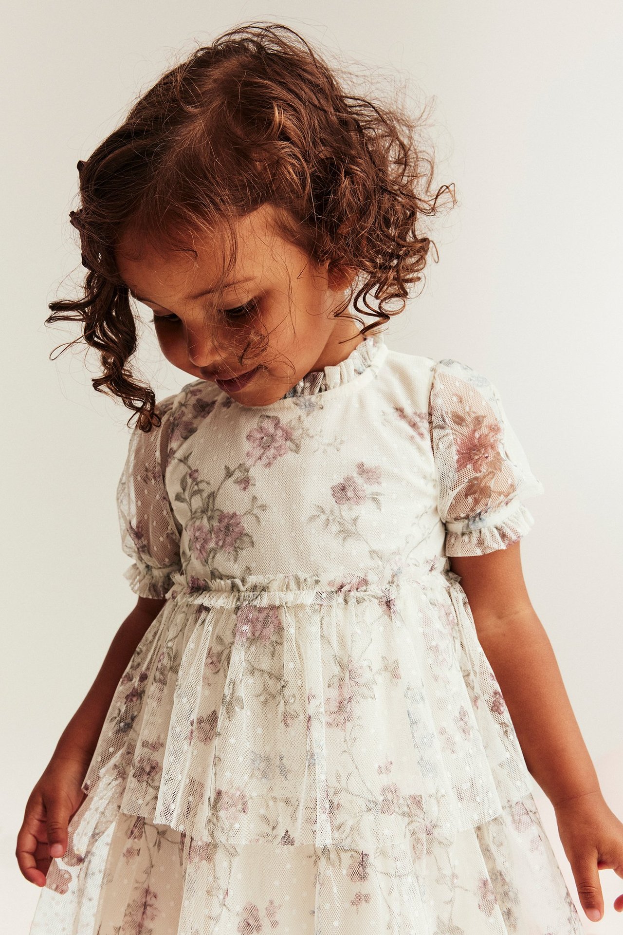 Nahaufnahme eines Kindes in hellbeigem Blumen-Mesh-Kleid mit Rüschen, Puffärmeln und Stufenrock.