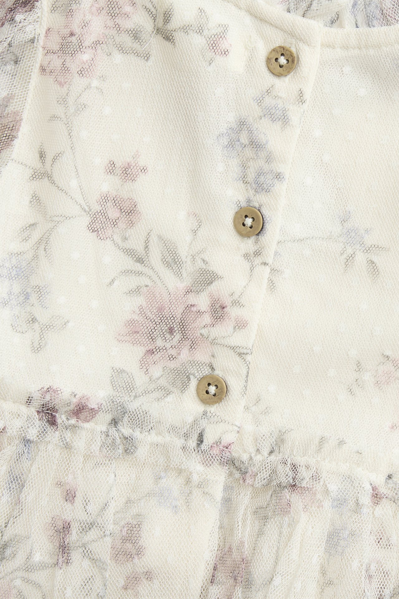 Close-up of a light beige floral mesh dress with a dotted texture and three light brown buttons.
