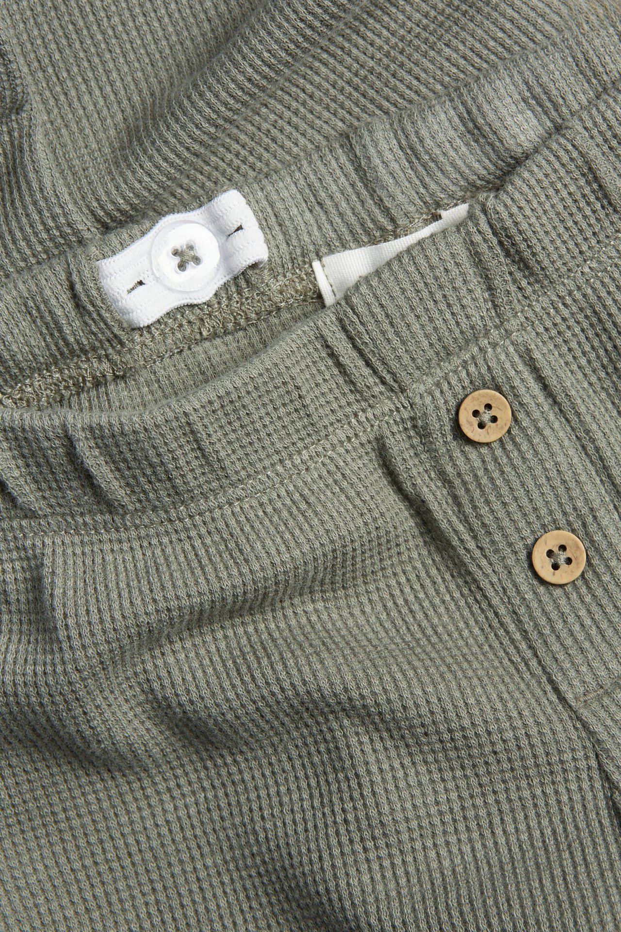 Nahaufnahme von dunkelgrünen Waffel-Leggings für Kinder, mit verstellbarem Gummizug und Holzknöpfen.