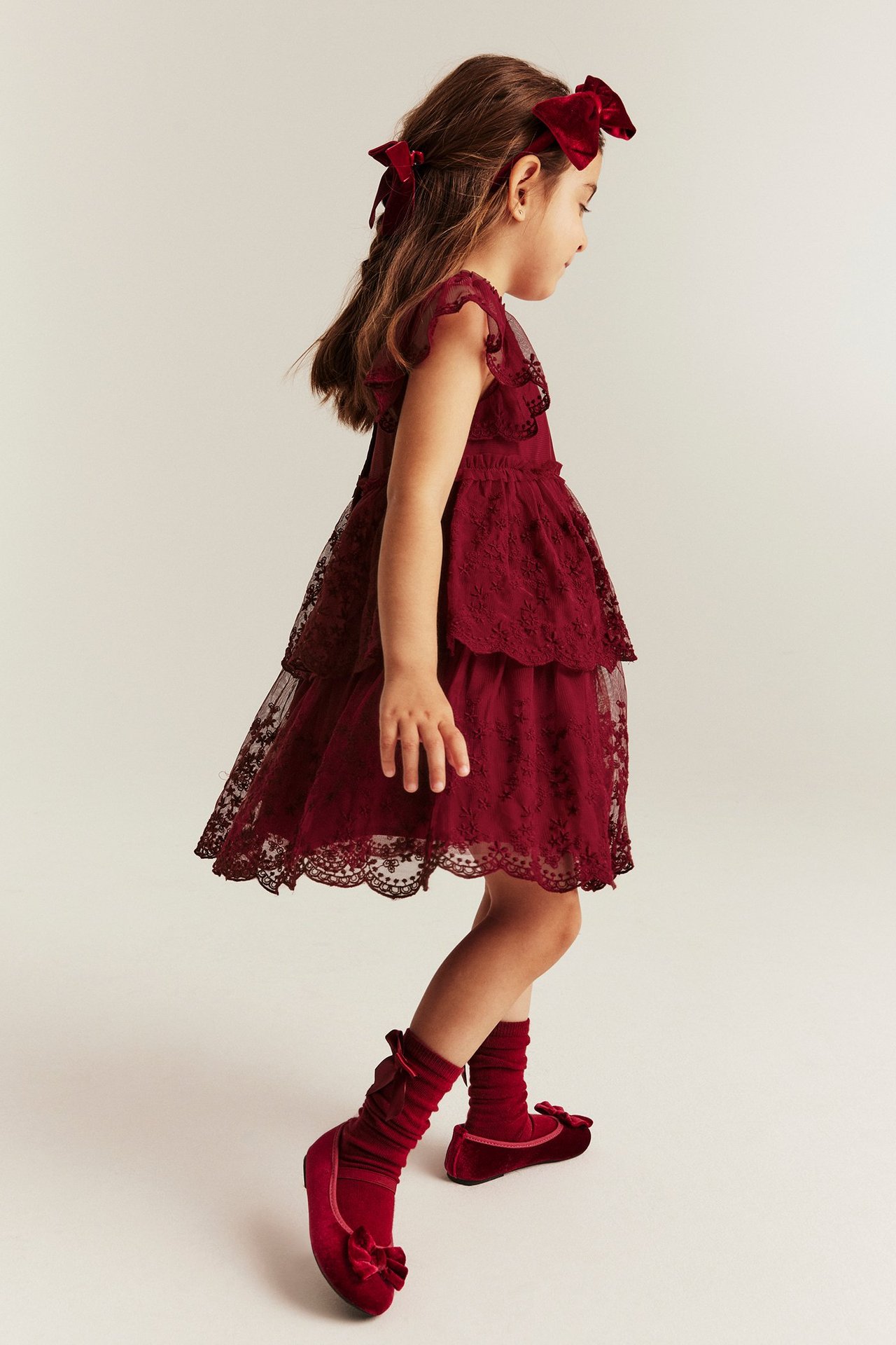 Girl in red mesh dress with embroidery, ruffle sleeves, back buttons, red shoes.