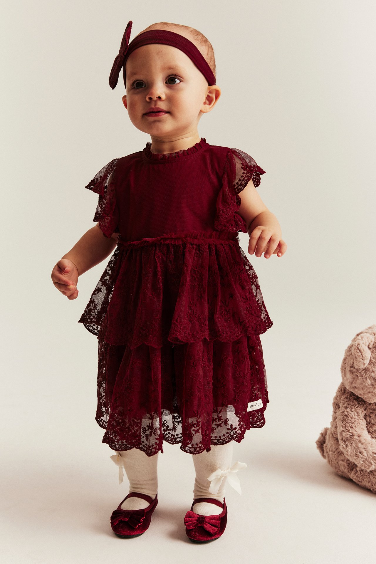Baby girl in a red mesh dress with embroidery, ruffles, and white tights.