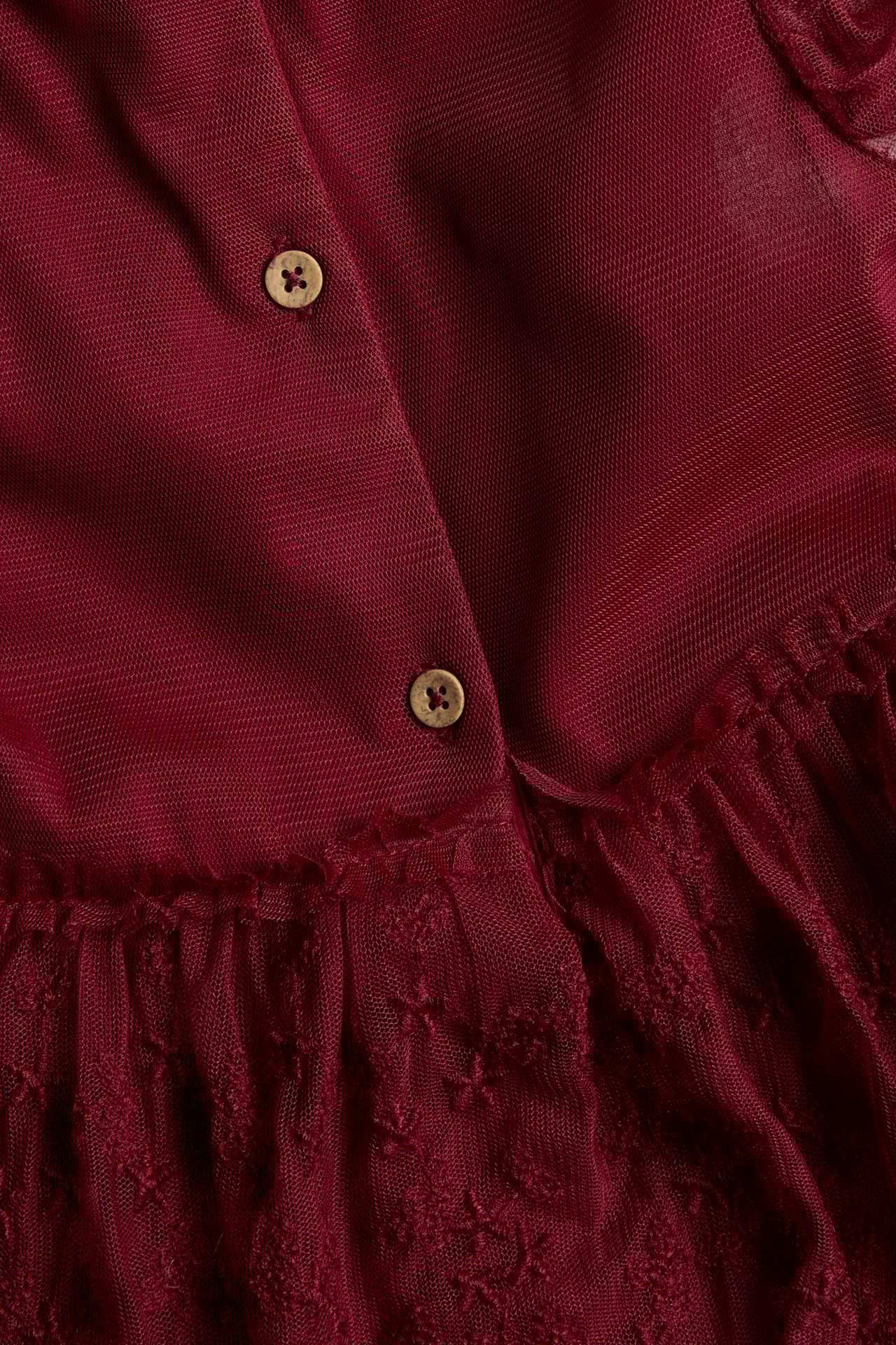 Close-up of a red mesh dress with embroidered detail and two wooden buttons.