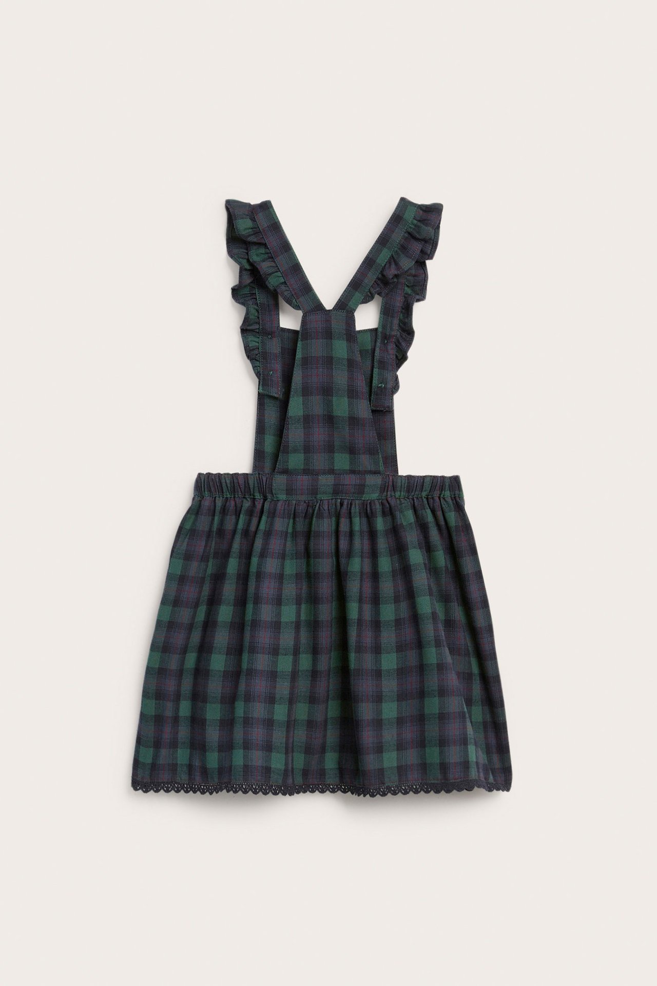 Front view of a kid's dark green and blue plaid pinafore dress with ruffled straps and lace trim.